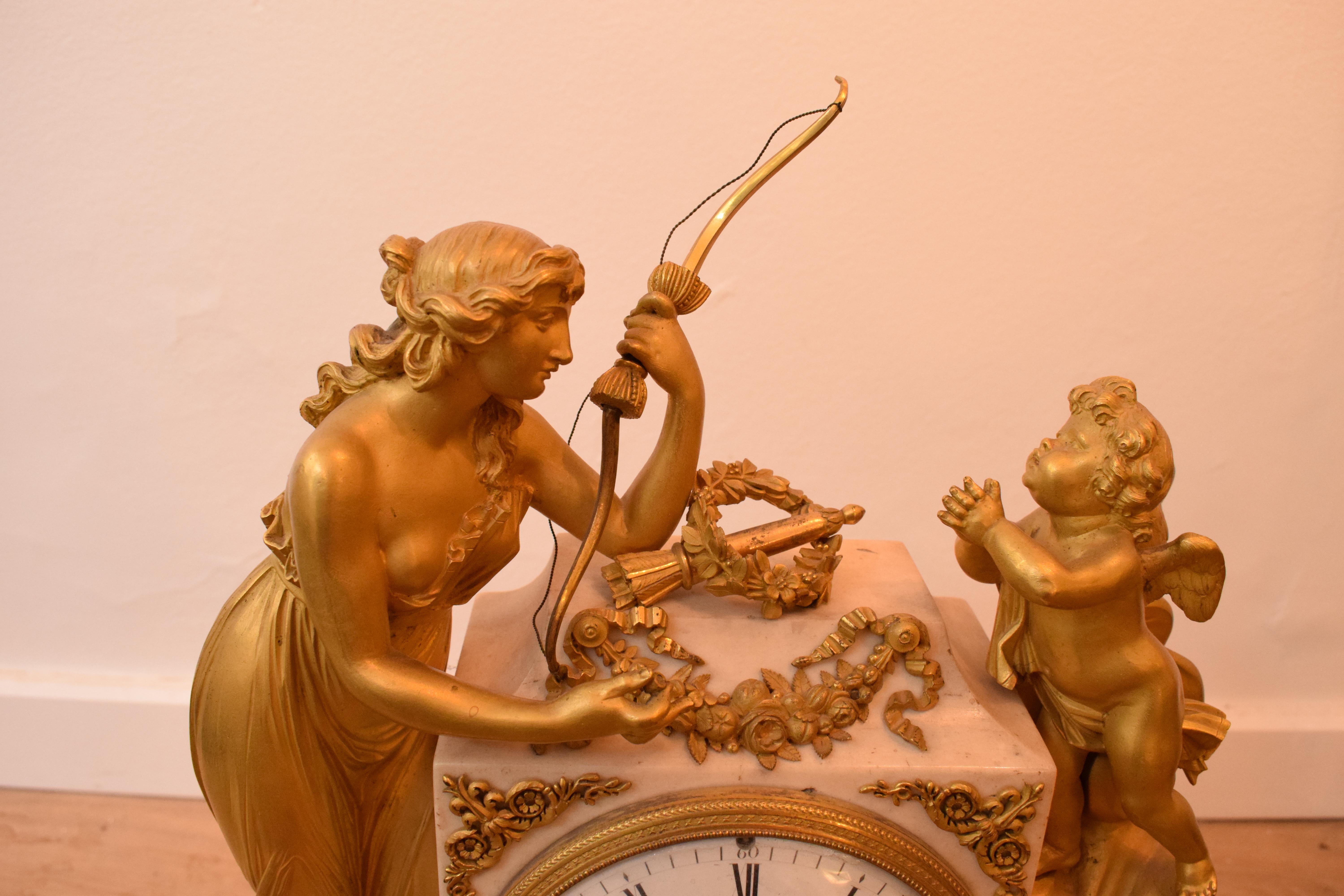 Pendule Borne d'époque louis XVI en bronze doré ciselé et marbre blanc de carrare , composée d'une pendule borne centrale en marbre à grand cadran émaillé, mouvement de Rolin L' Ainé à Paris, encadrée par une jeune femme à l'antique avec un arc et