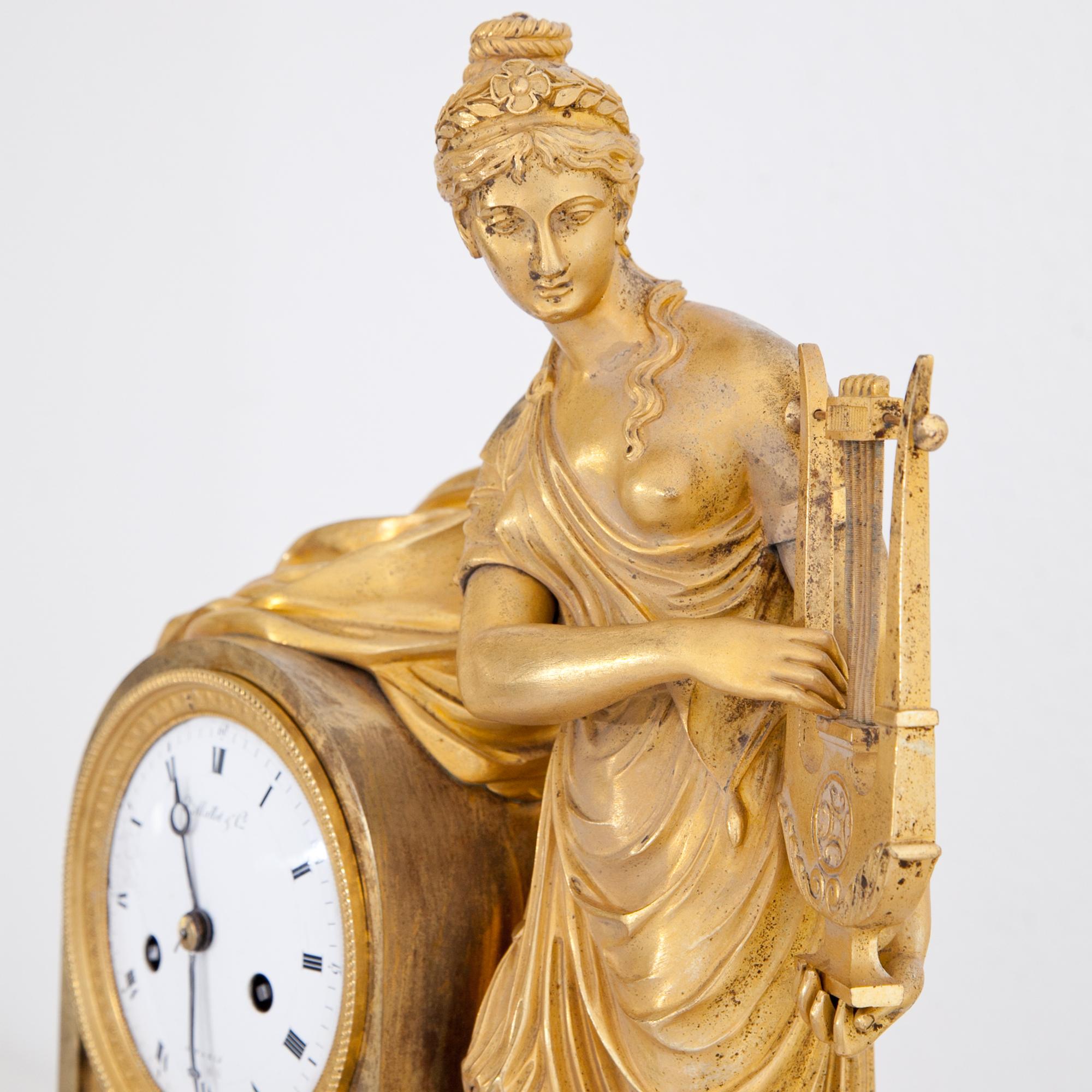 Pendule clock out of gilt bronze, standing on a grey marble base, depicting the allegory of music as a young female, playing the lyre. The enamel clockface shows cracks and is inscribed “Mallot & Cie à Paris”.