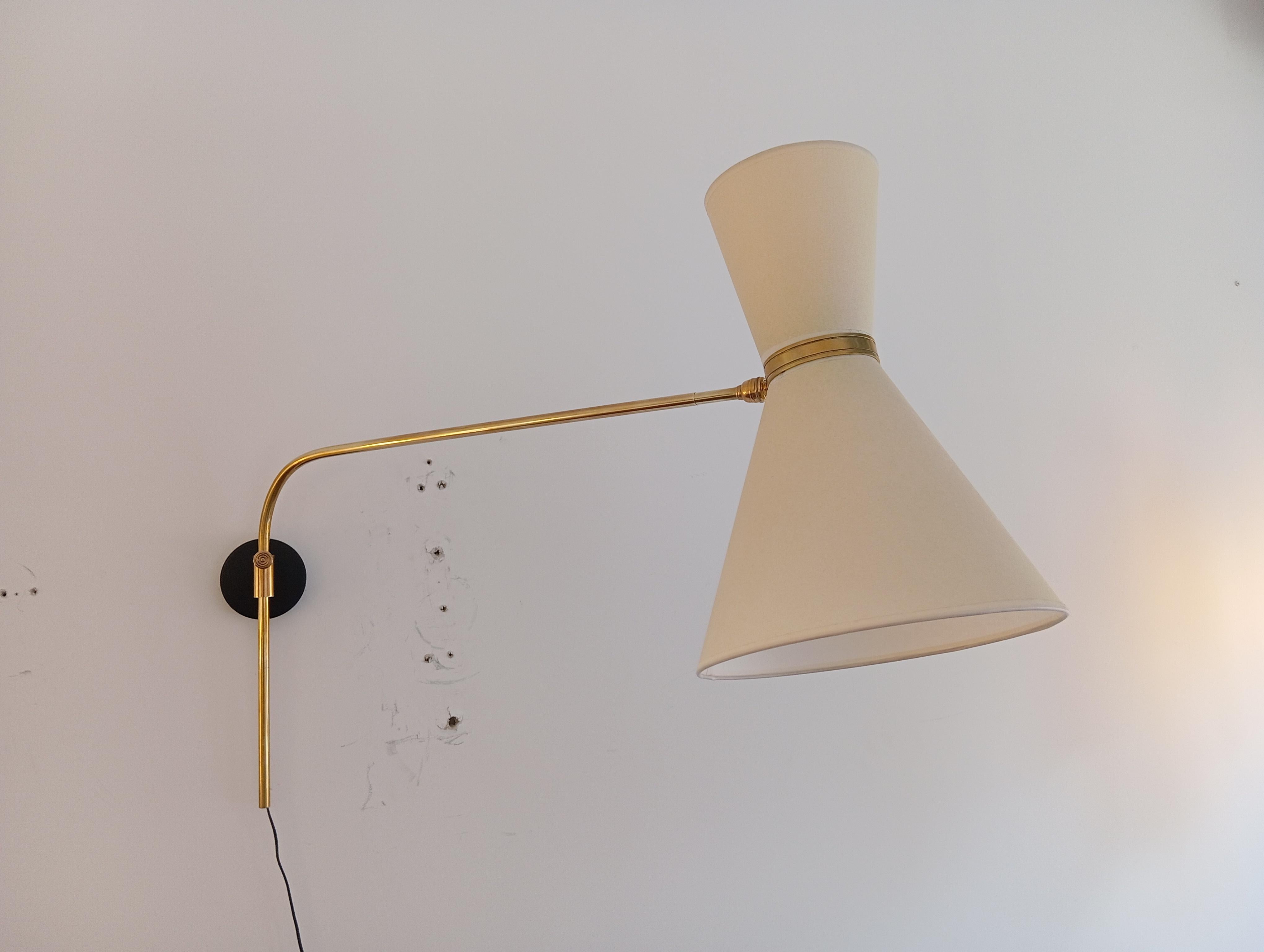 Aplique de latón, compuesto por una base cilíndrica de metal lacado en negro, sobre la que se monta un brazo luminoso de latón, regulable de izquierda a derecha.
El brazo puede extenderse en longitud.
Una doble pantalla cónica difunde la luz, y la