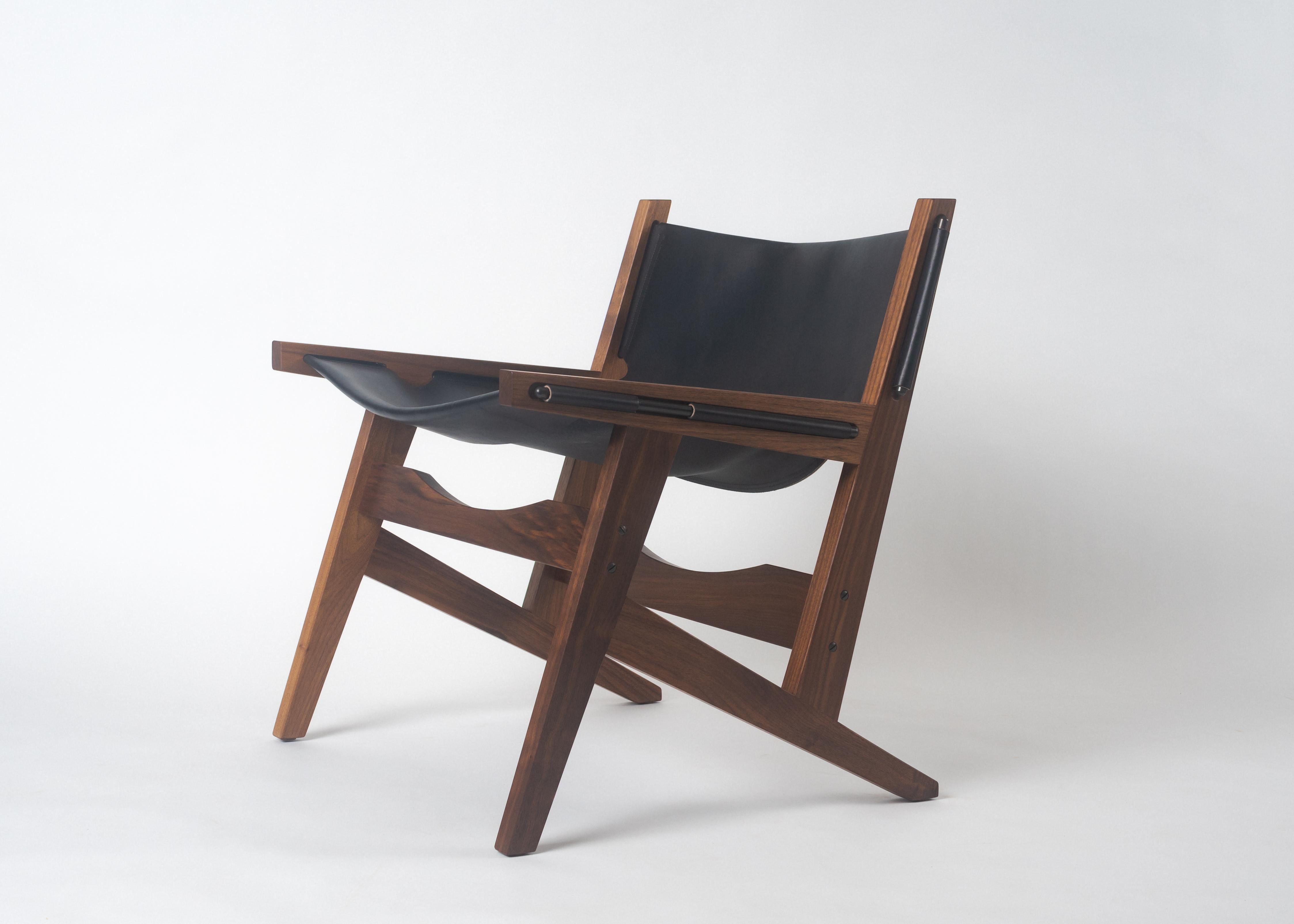 Der Phloem Studio Peninsula Sessel ist ein moderner, zeitgenössischer Sling-Loungesessel aus Leder. Der handgefertigte Rahmen aus massivem Nussbaumholz hält die schwere Zaumzeug-Lederschlaufe mit solide geformten, freiliegenden Messingstäben in