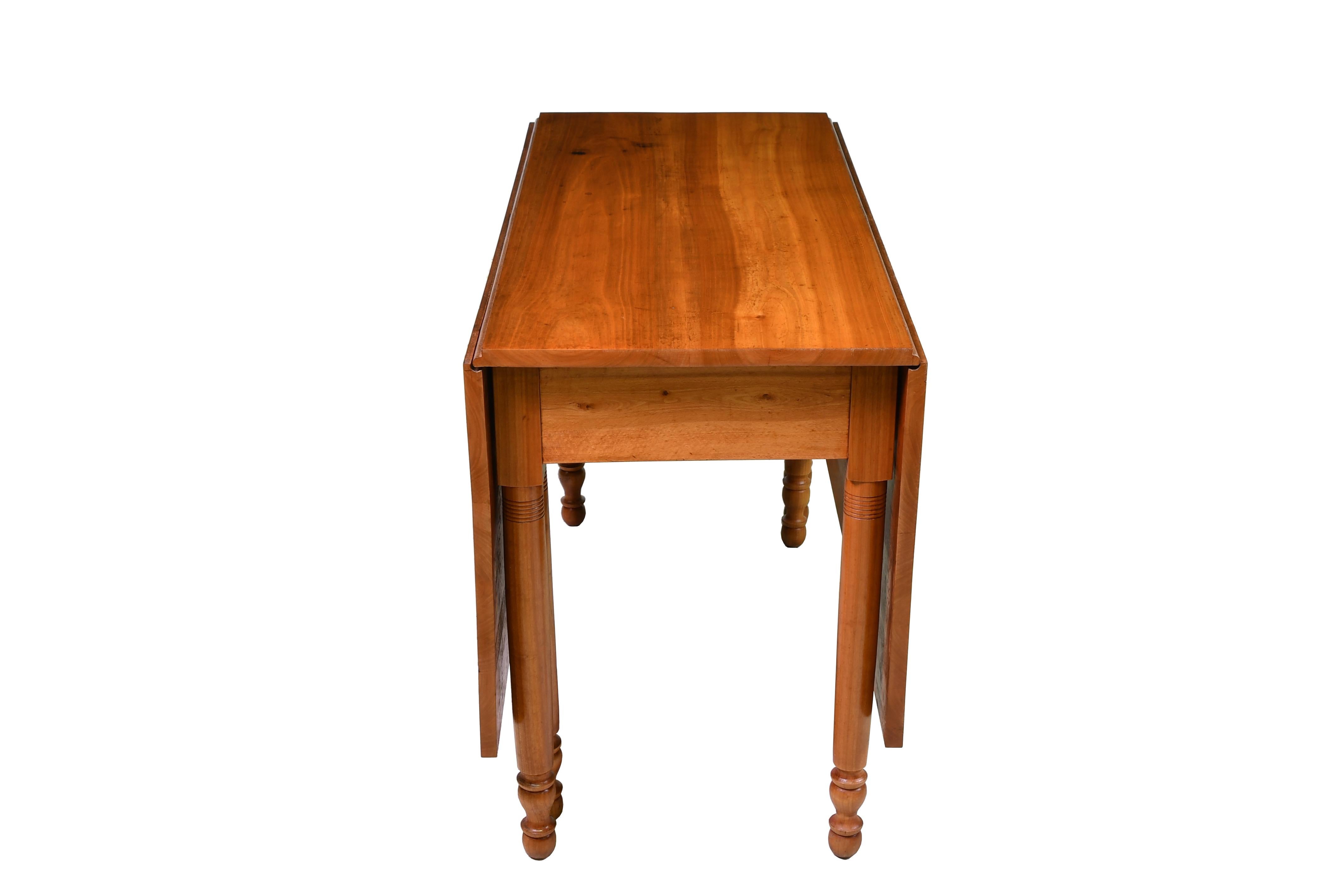 An exceptional American Sheraton dining table from southeastern Pennsylvania, made of fine solid cherry that has fine figuring & is a light amber color. When open, the long drop-leaves are supported by gate legs with turned cylindrical legs, with