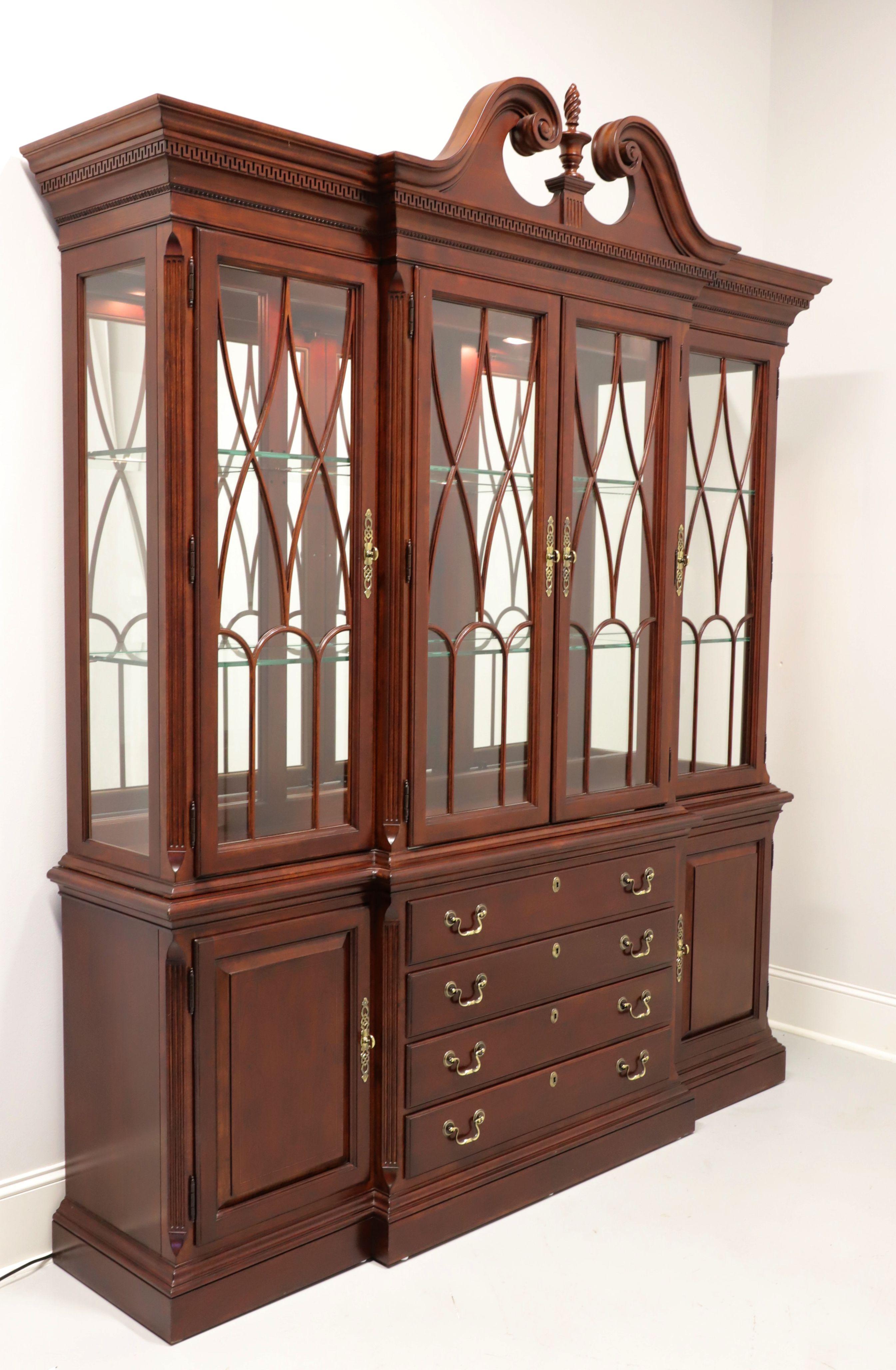 A Traditional style breakfront china cabinet by Pennsylvania House. Cherry with brass hardware, crown & dentil moulding, pediment to top with center finial, glass doors with fretwork panes, and ogee edge to solid base. Upper cabinet features Dual