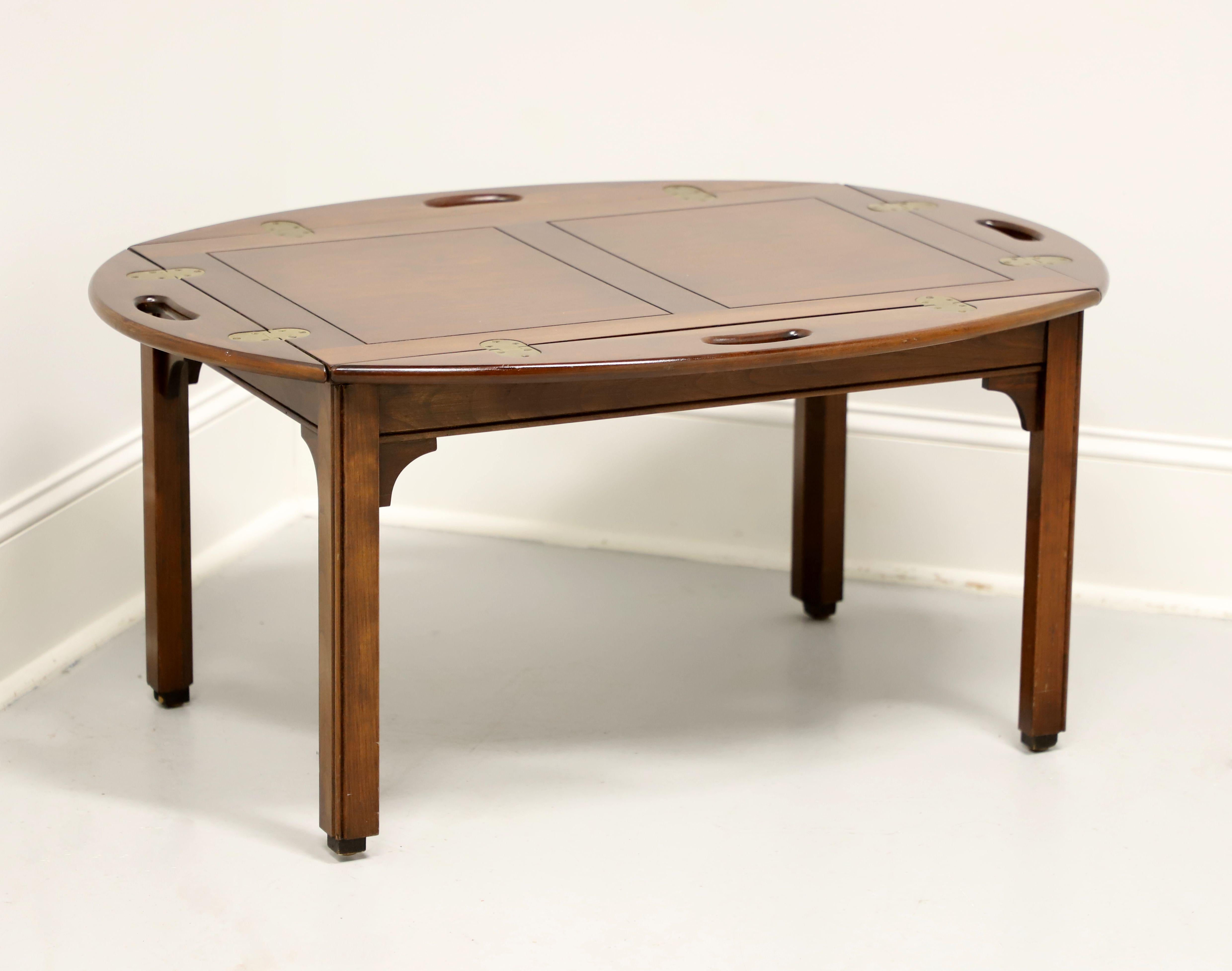 A Chippendale style butler's coffee table by Pennsylvania House. Solid cherry wood with brass hinge hardware, banded top, carved straight legs, and block feet. Features four fold down sides with carved open handles creating an oval shape when down.
