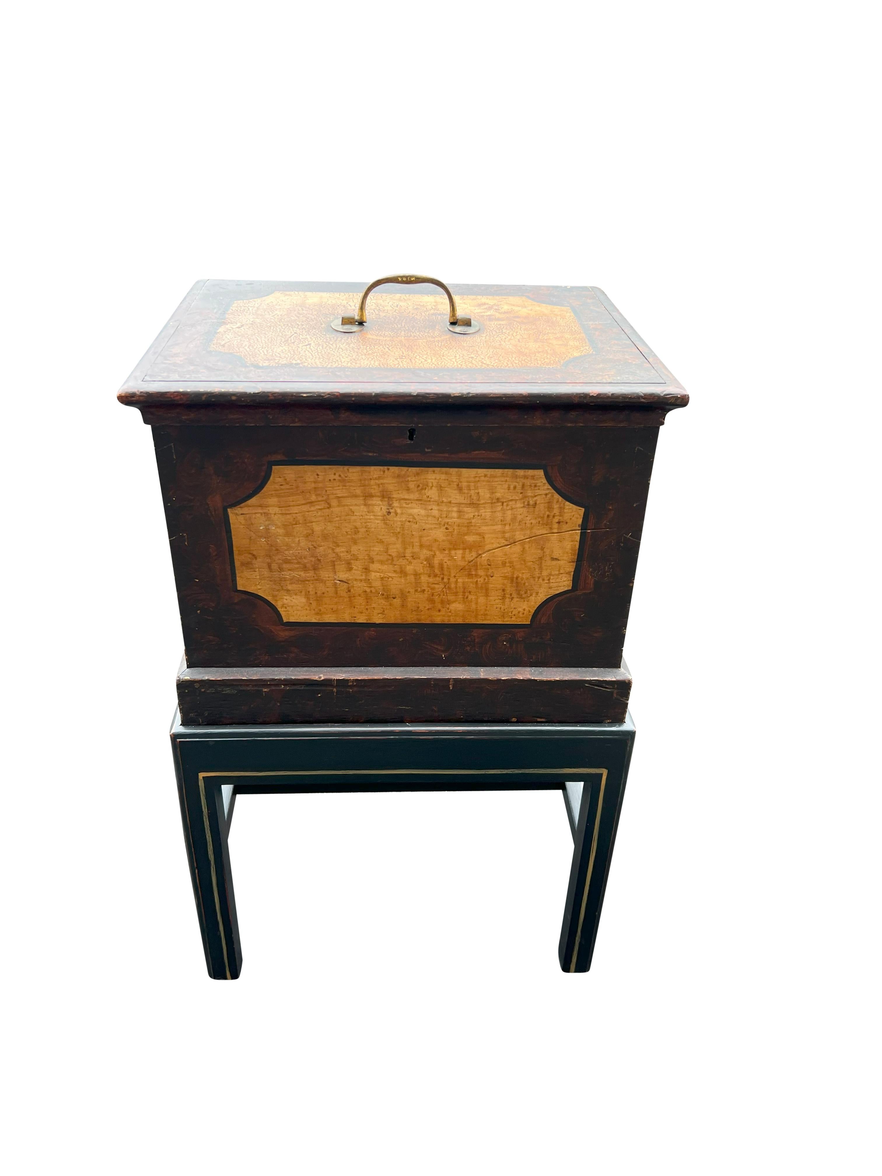 Square form with hinged lid with original brass bail handle. Faux bois decoration. The matt black painted wood base with square section legs and H form stretchers.