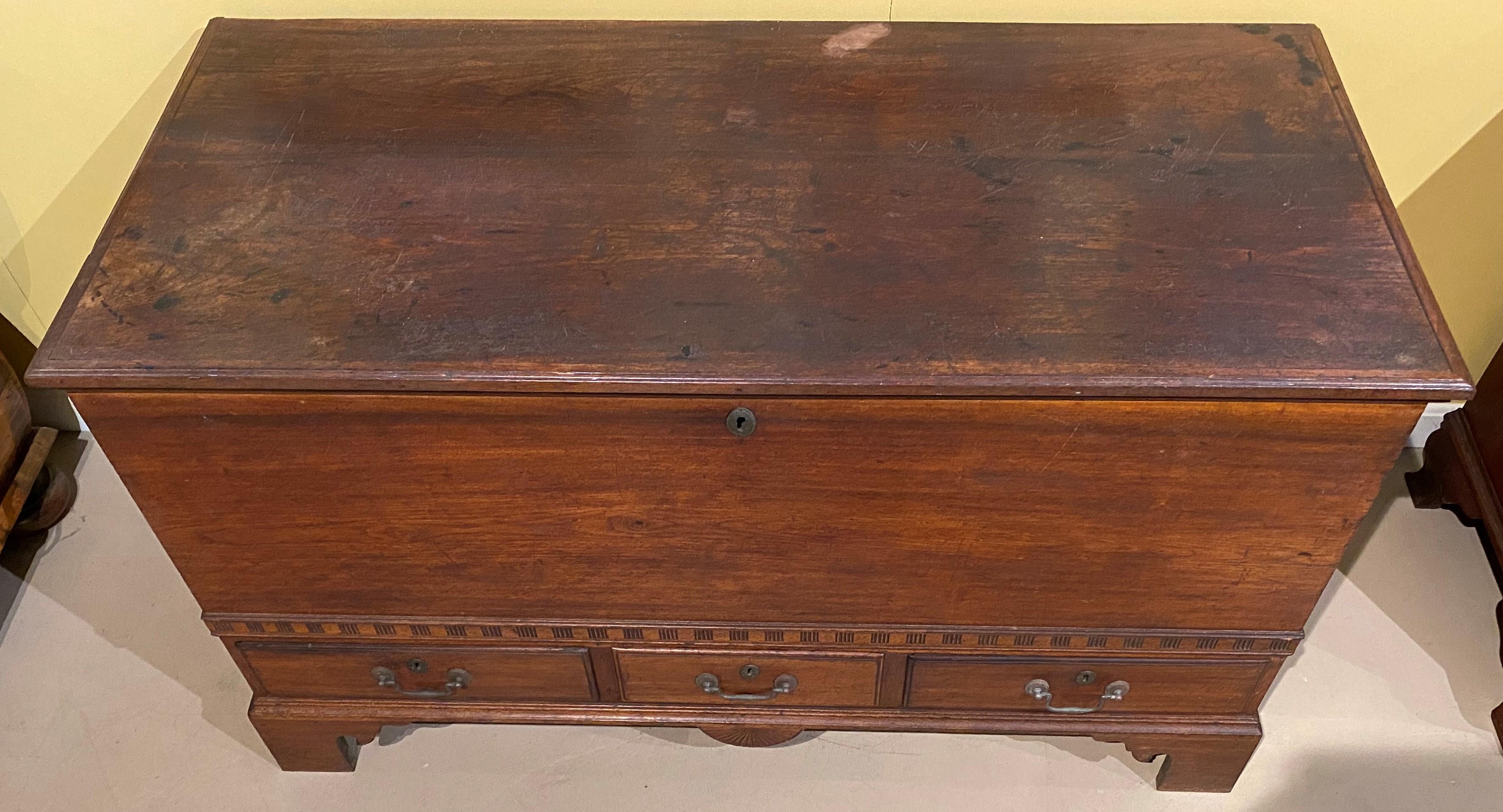 A fine example of a country walnut country blanket or dower chest with three fitted drawers, an interior till in old red, dovetailed corners, on a carved bracket base with center carved radial fan drop. A decorative carved band runs around the front