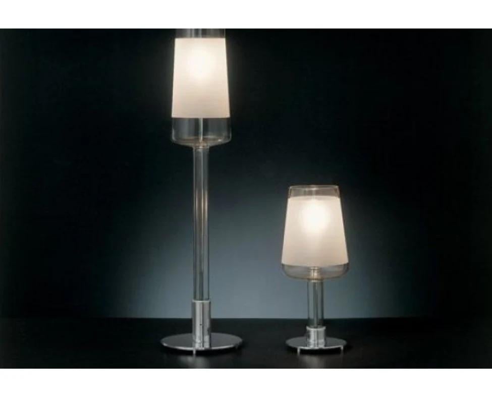 The modern table lamp is a great mounted luminaire for halogen lighting. The shade is in transparent glass. There is a sandblasted band to cover the bulb. This table lamp will certainly brighten any atmosphere.  