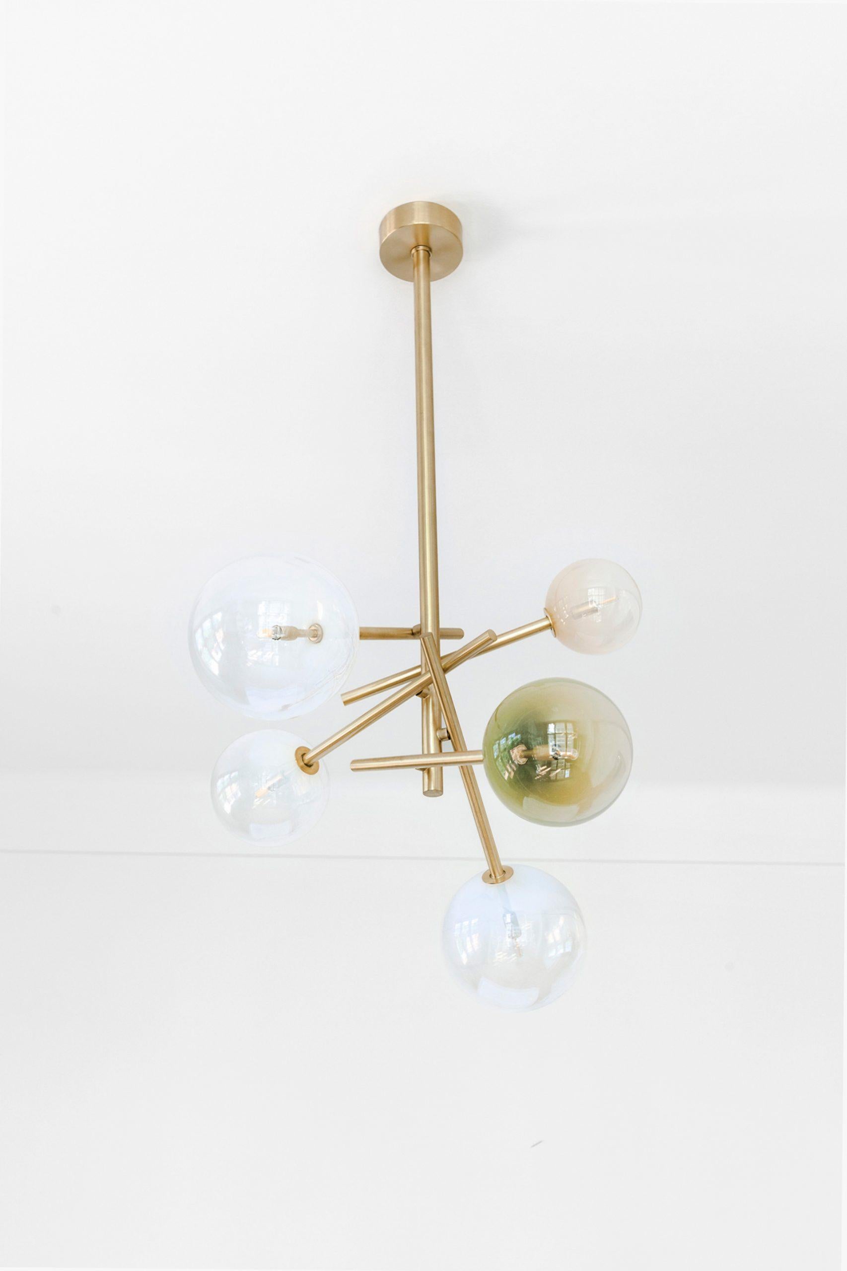 Penta pendant light by Dechem Studio.
Dimensions: D 150 x H 200 cm.
Materials: brass, glass.
Available in different glass colors.

The chandelier combines a deconstructed and newly arranged brass structure with hand-blown glass shades in