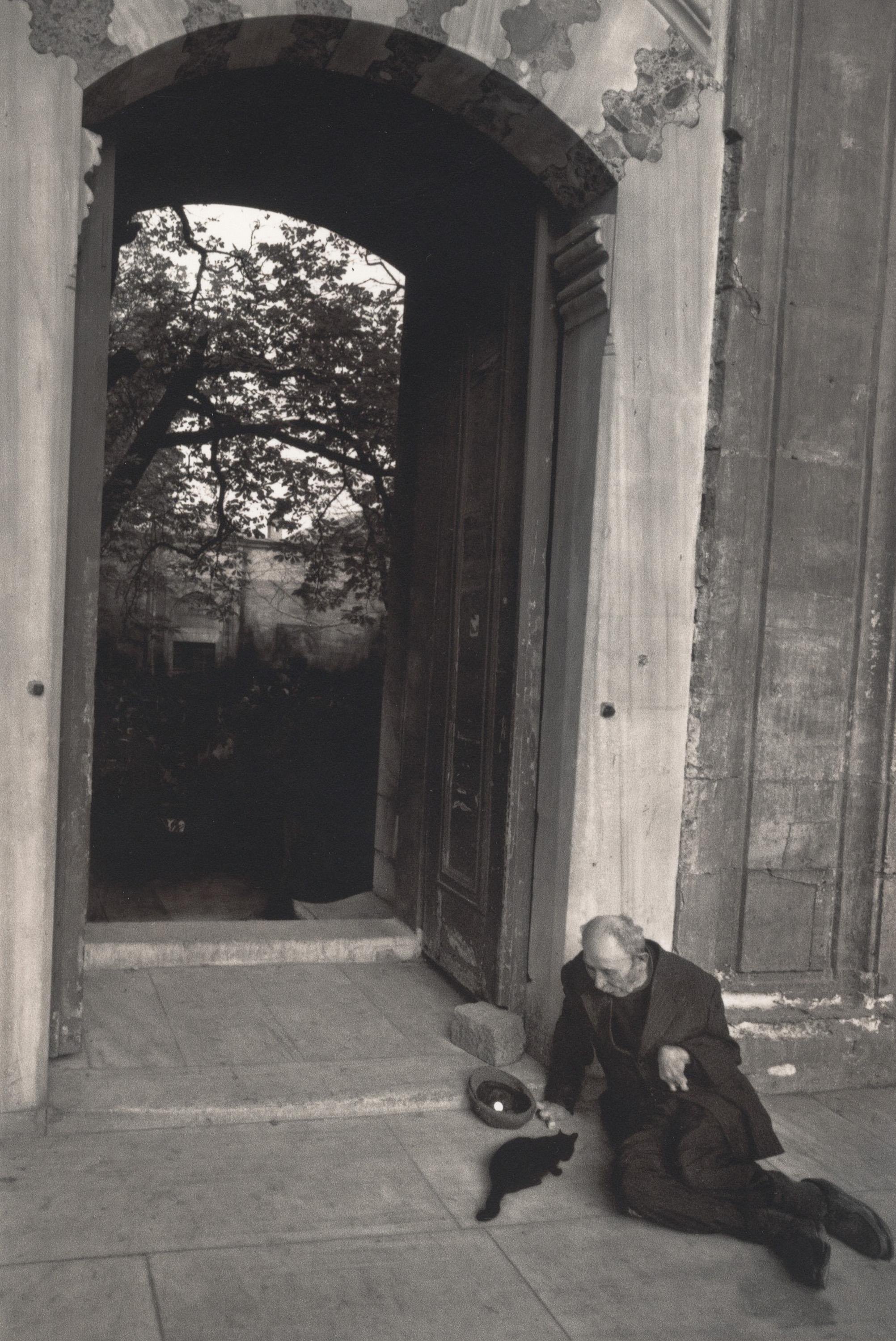 Landscape Photograph Pentti Sammallahti - Istanbul, Turquie (Un homme se penchant près d'une porte, nourrissant un chat)