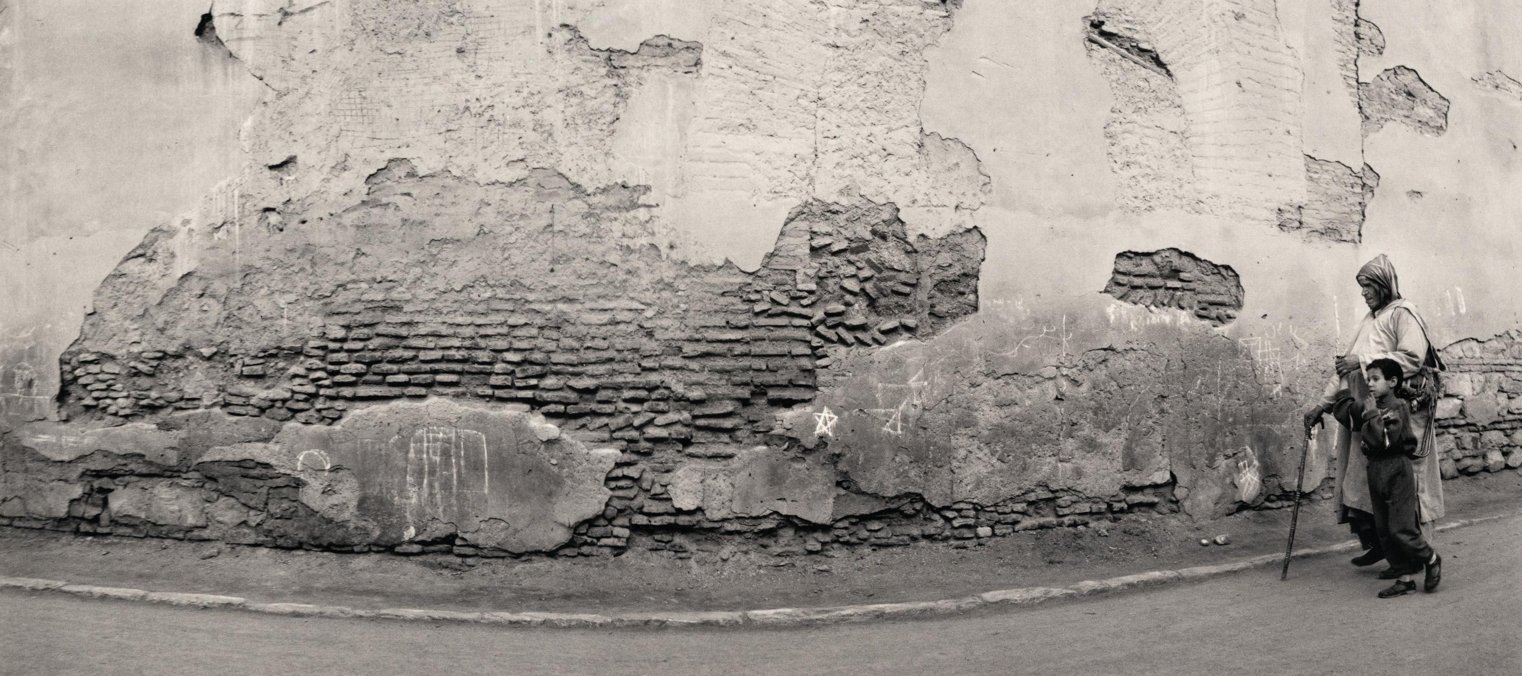 Pentti Sammallahti Black and White Photograph - Marrakech, Morocco (Boy & old man w/cane, crumbling plaster wall)