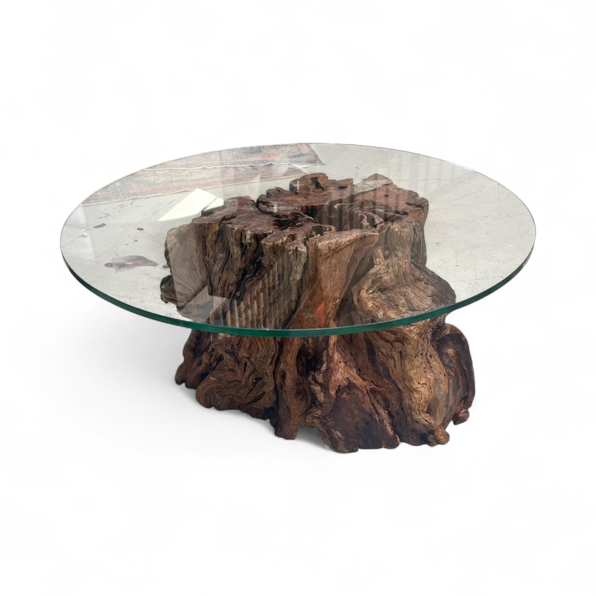 A sculptural pepper wood base with organic twists and textures anchors this striking coffee table, topped with a sleek round glass surface. The natural grain and rich tones of the wood bring warmth and character, blending rustic artistry with modern