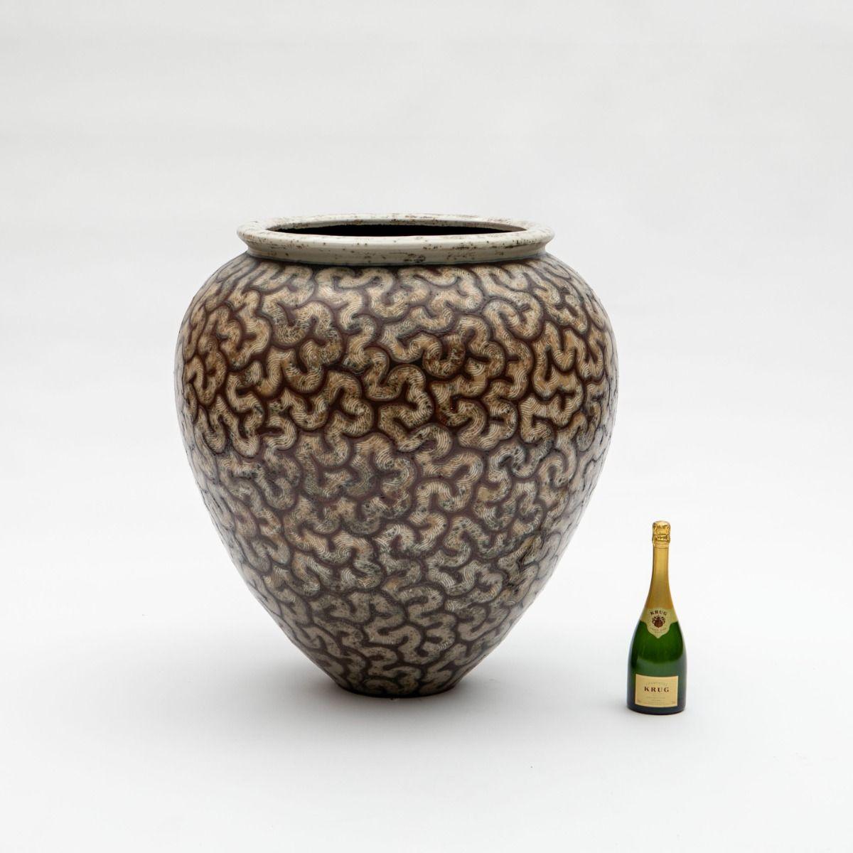 An impressive, colossal floor vase crafted in glazed stoneware, featuring organic, geometric patterns both in the glaze and in relief. The labyrinth-like pattern adds striking depth to the surface. The glaze is in beautiful shades of light red,
