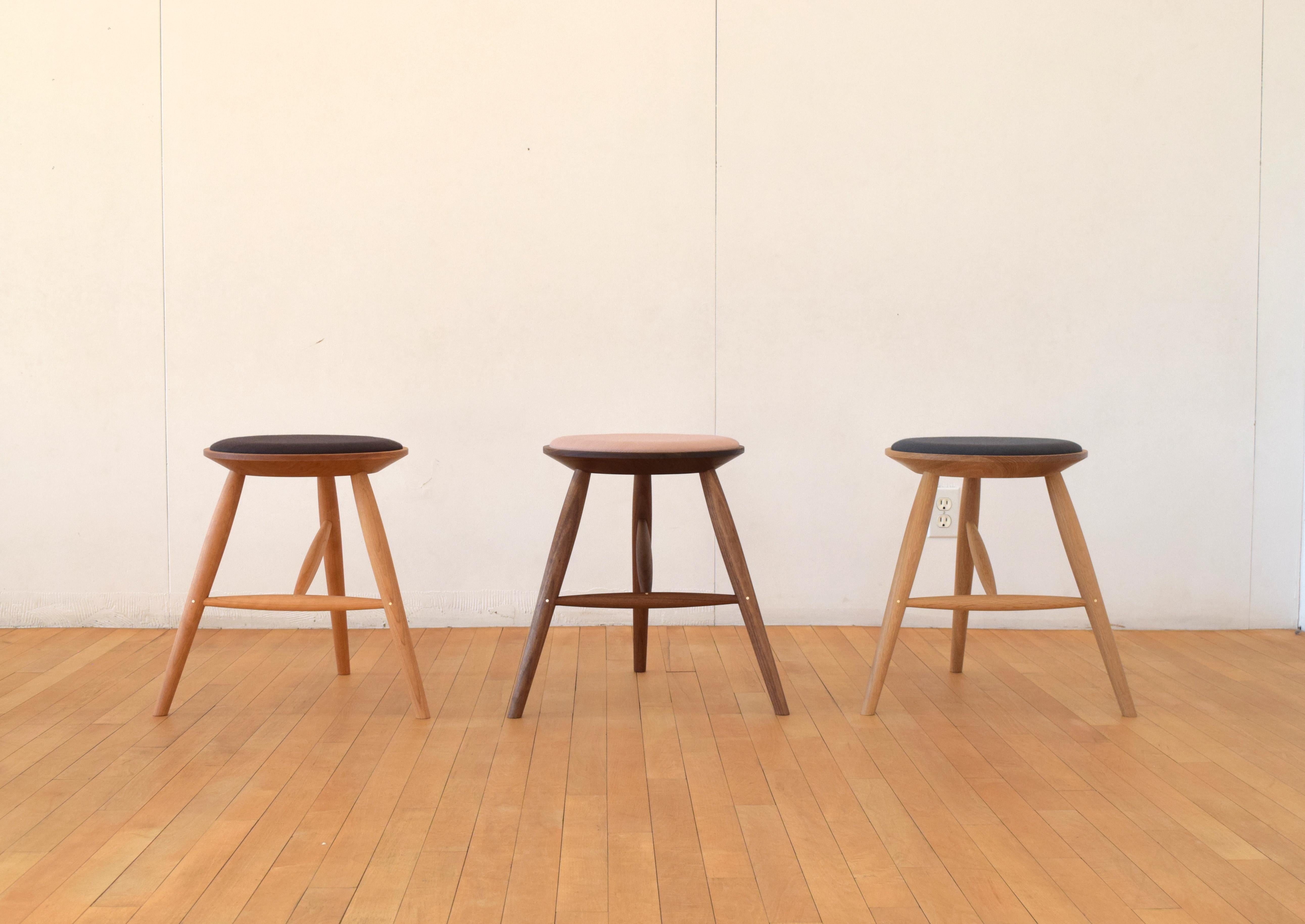 Perch stool is a solid wood, three-legged seating option with an upholstered seat cushion. The stool features traditional woodworking construction including mortise and wedged tenon joinery and brass pins, and is upholstered with 100% wool fabric.  