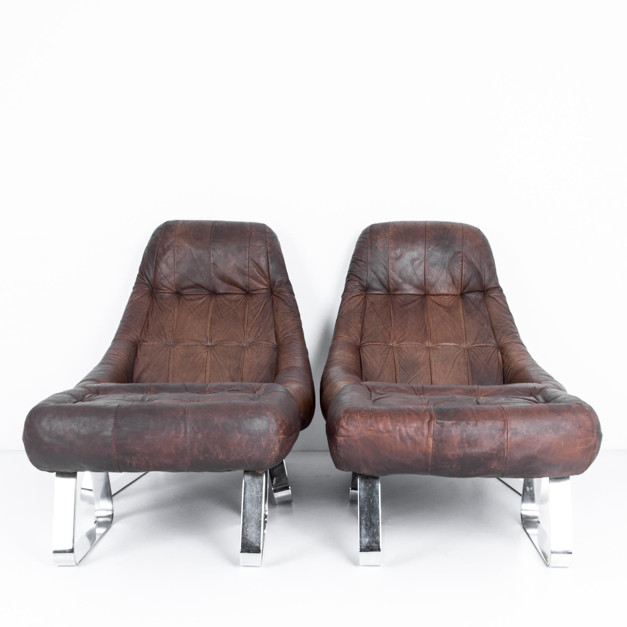 A pair of leather armchairs with matching ottomans by Brazilian designer Percival Lafer. Elegantly aged, the patina highlights a rich dark leather, elevated on chromed metal legs. The effortlessly clever design is captured in en-pointe material,