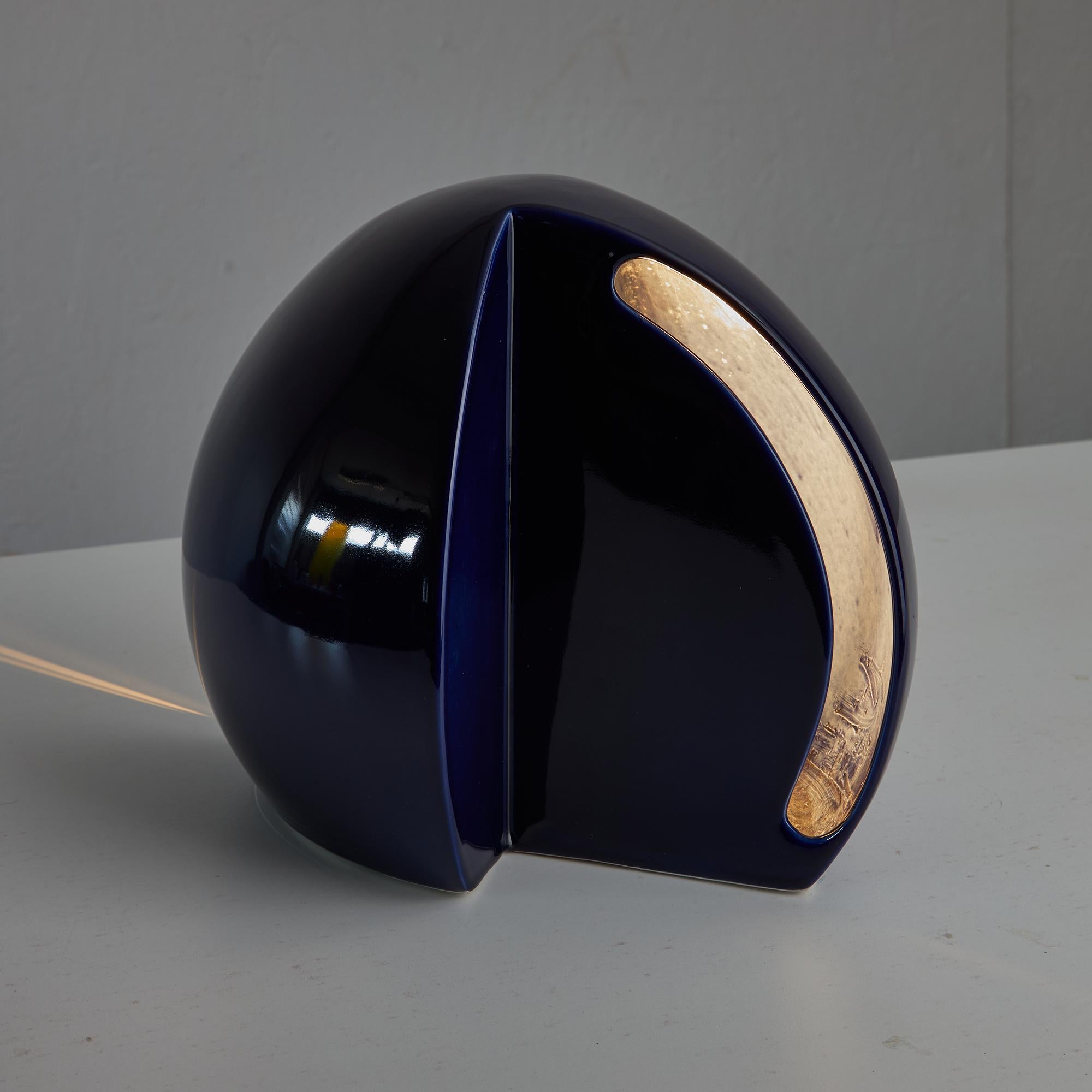 Questa lampada da tavolo emisferica in ceramica, sorprendente sia nella forma che nella finitura, conferisce un'eleganza scultorea e un'illuminazione d'atmosfera a qualsiasi interno. Realizzato con un ricco smalto blu intenso, il pezzo presenta due