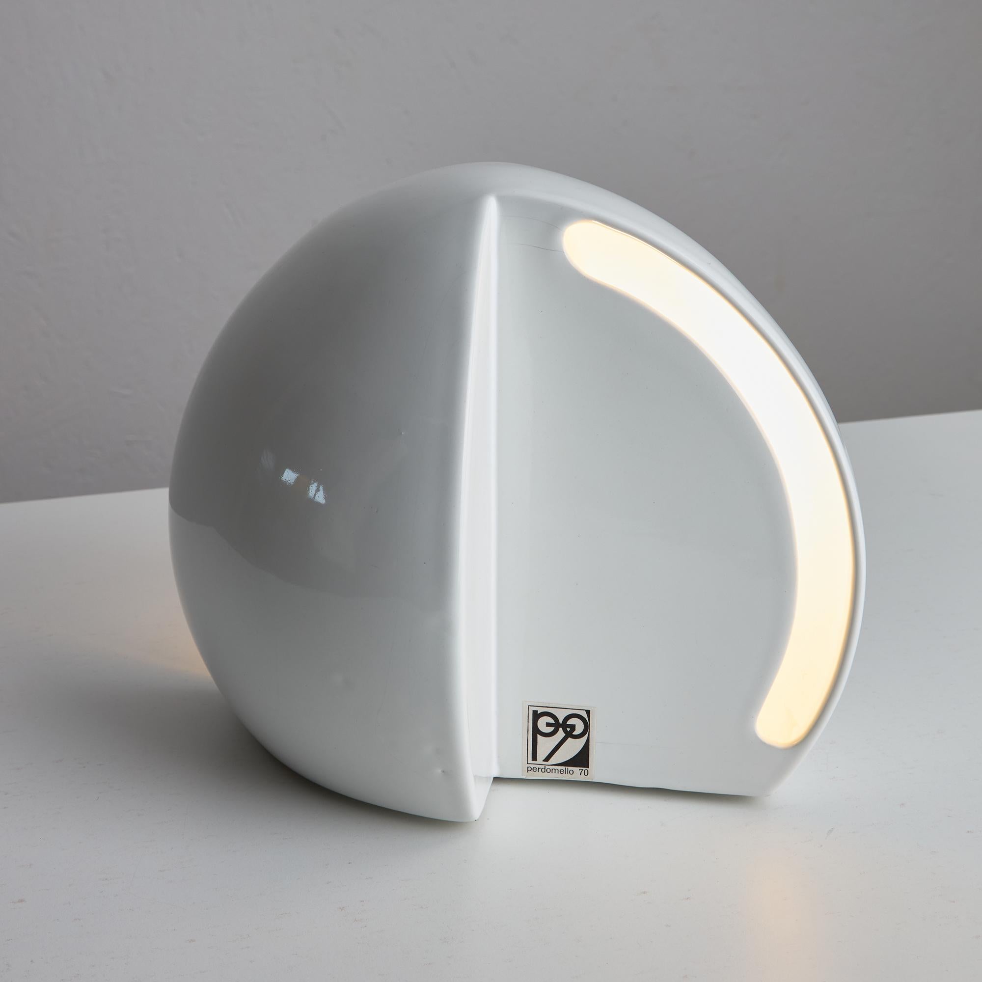 This sculptural ceramic table lamp features a refined hemispheric form finished in a smooth, white glaze. Designed with two elongated lateral openings, the piece casts a patterned wash of light, creating a soft, ambient glow and adding a layer of