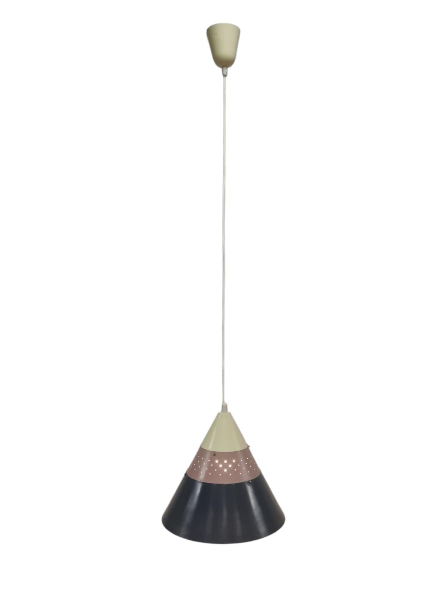 Un pendente da soffitto a forma di cono, perforato e stratificato, realizzato da Maria Lindeman per Idman. La lampada è composta da tre strati di metallo di colori diversi che vanno dal grigio scuro al beige brik e al beige chiaro. La lampada è