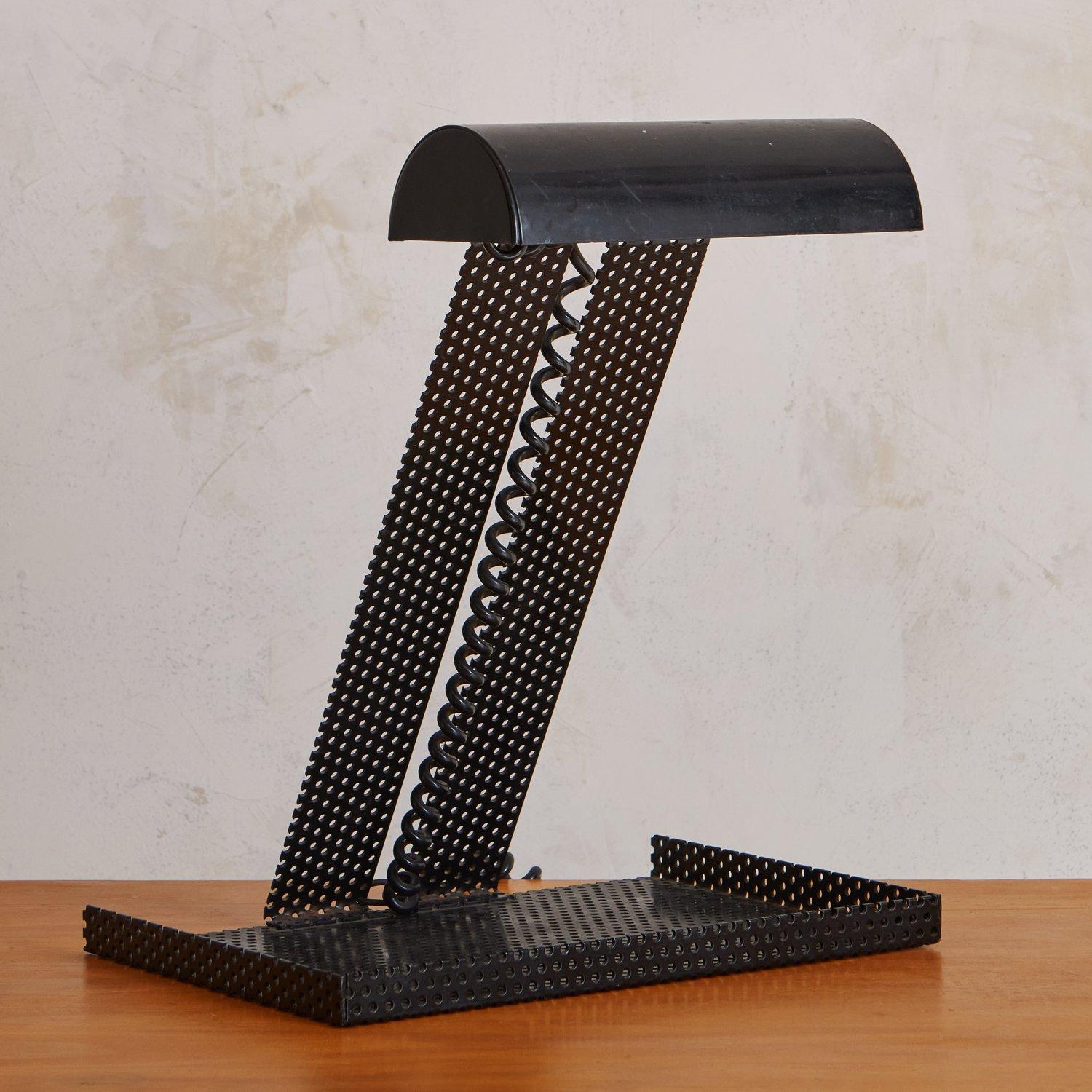 A sculptural black perforated metal table lamp sourced in France. This lamp has an oversized rectangular base perfect for storing your treasures and desk supplies. It has a cylindrical demilune shade and black coiled cord. 20th Century.