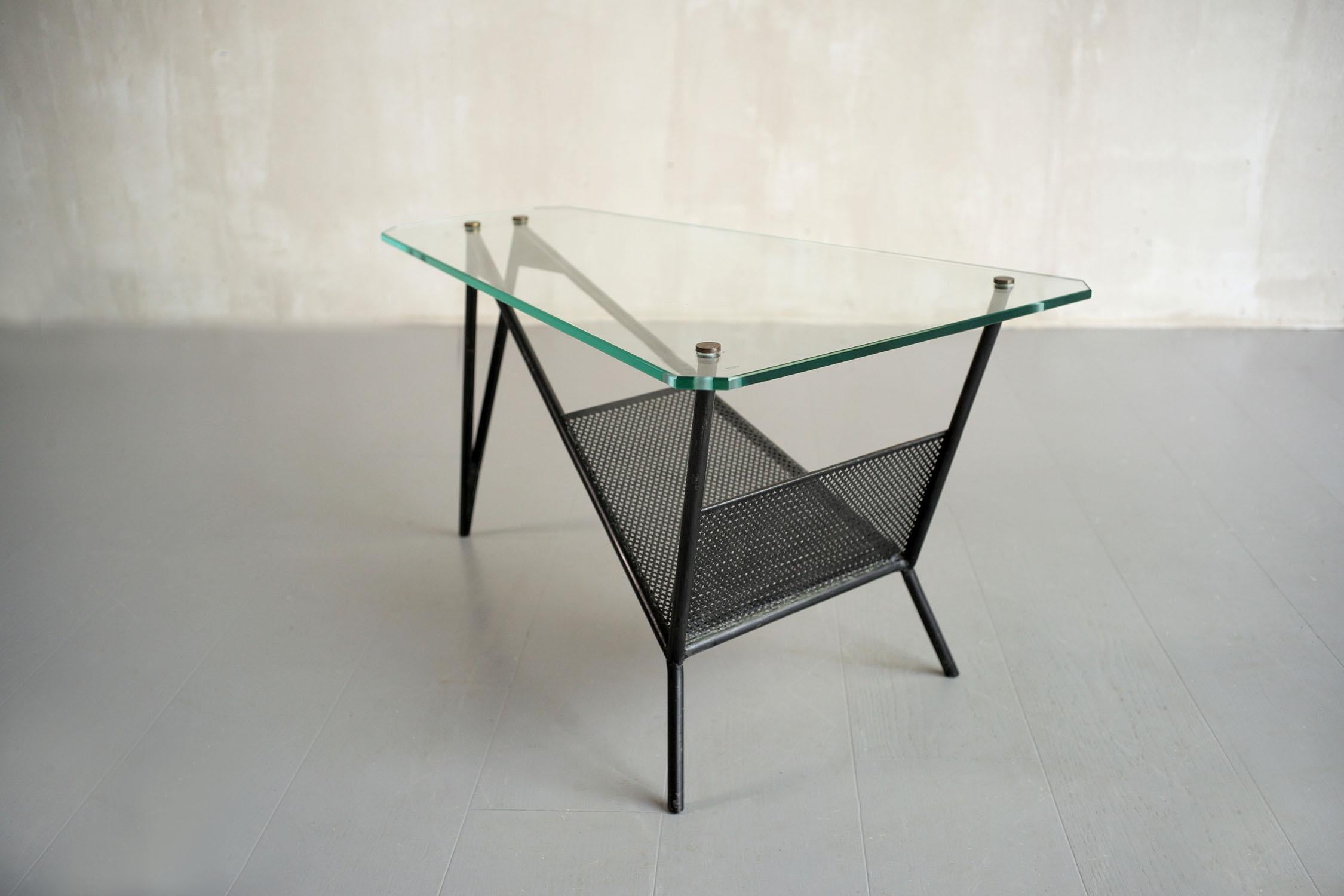 Coffee table in black lacquered metal attributed to Robert Mathieu, France 1950. The tripod base receives a perforated metal newspaper shelf, the glass top is in the shape of a trapezoid with cut sides, fixed by large blind nuts in patinated brass.