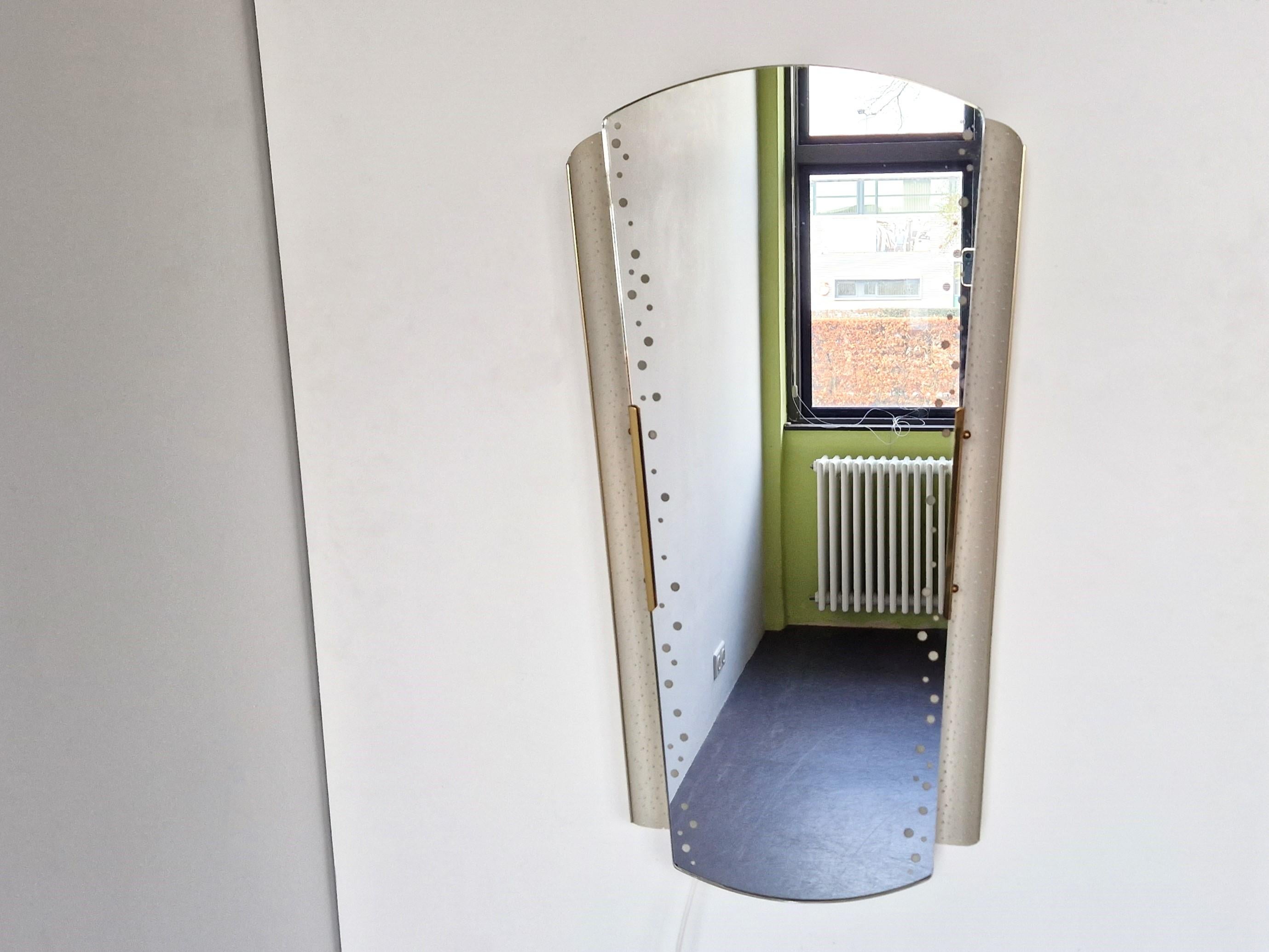 Dieser beleuchtete Spiegel wurde in den 1950er Jahren von Ernest Igl für Hillebrand Lighting in Deutschland entworfen. Ein schöner Spiegel und Blickfang! Der perforierte, cremefarbene Metallrahmen, die Messingdetails und die Punkte im verspiegelten