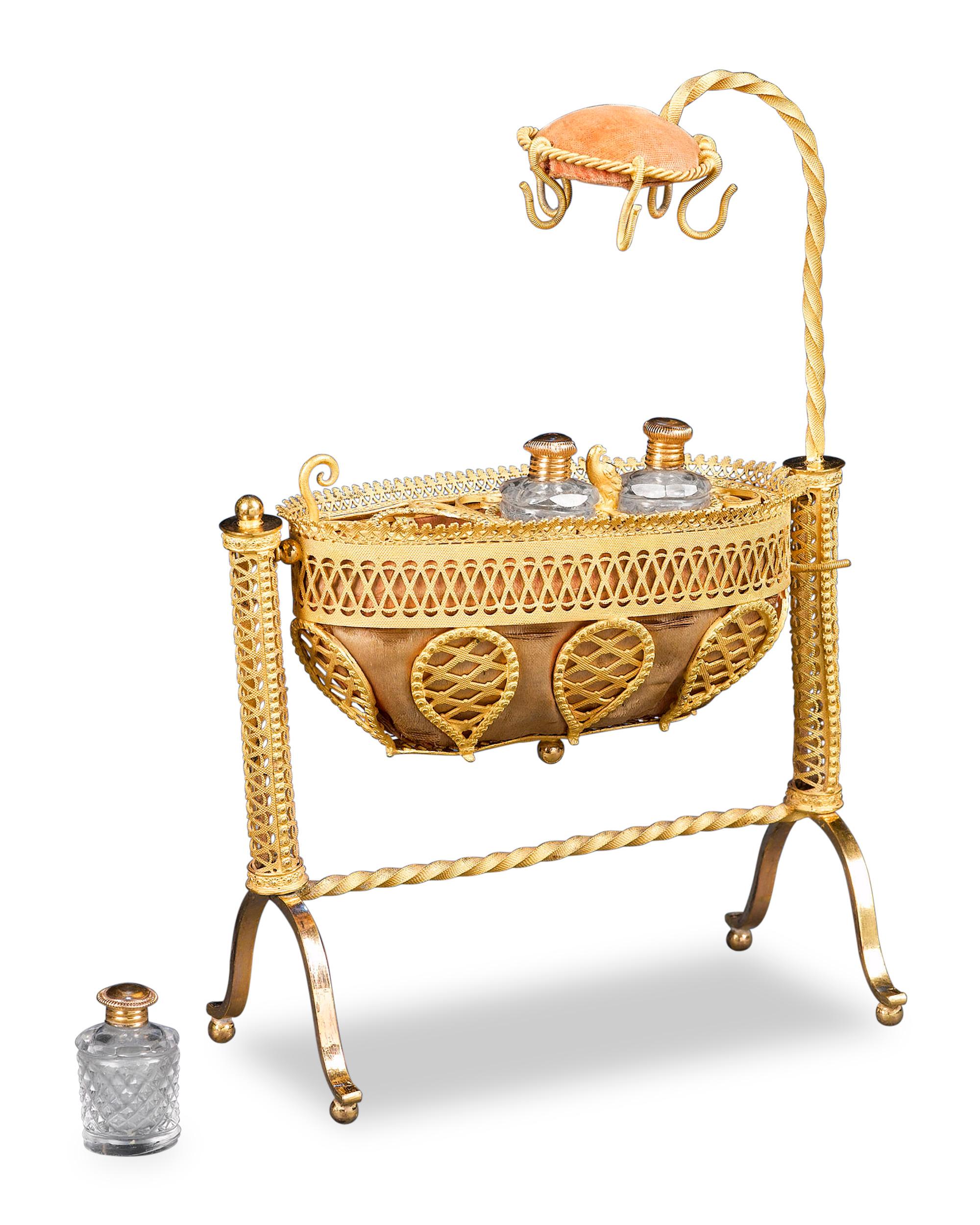 This rare and intricate French perfume bears precious cargo in its bassinet-form design. Crafted of lace-like doré bronze with silk and velvet accents, the swinging cradle holds three cut crystal perfume bottles, each with a gilt bronze cap and