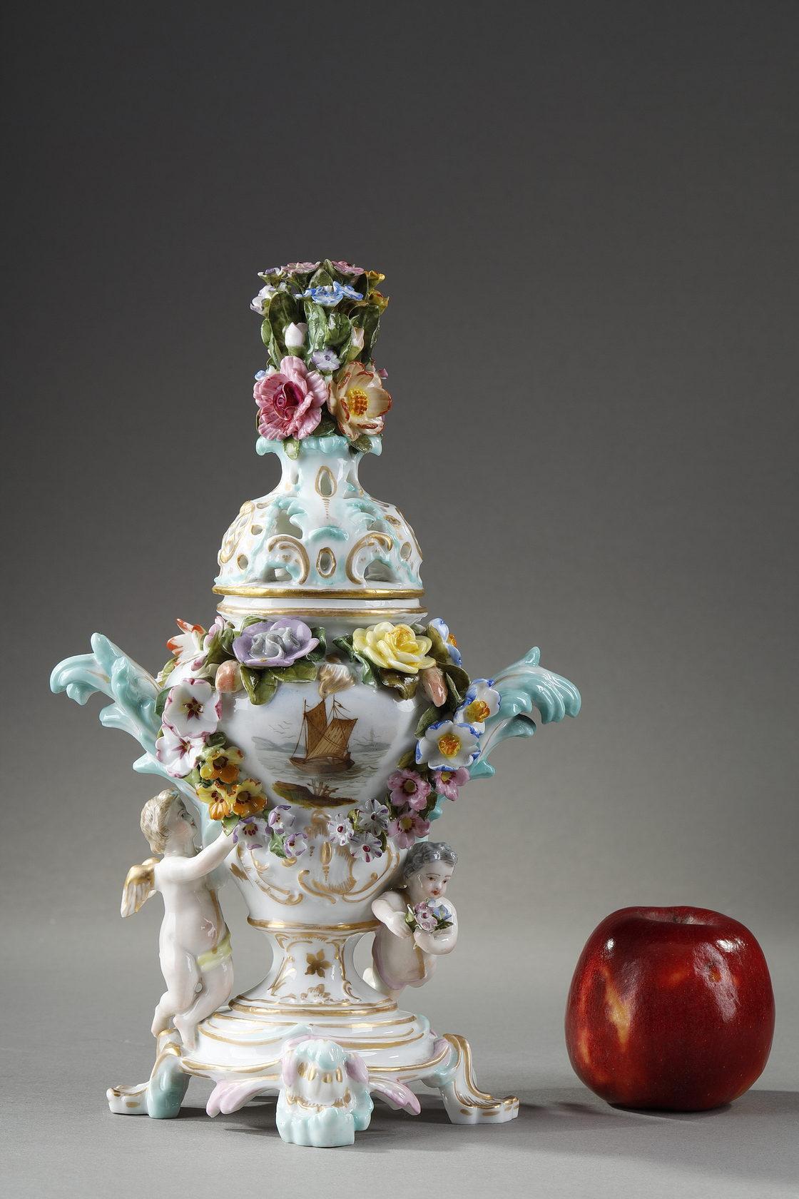 Meissen polychrome and gilt porcelain potpourri. It takes the form of a vase with an openwork lid topped by a bouquet of porcelain flowers. The body, flanked by two moving handles, is decorated with a ship and flowers in relief. The foot is animated