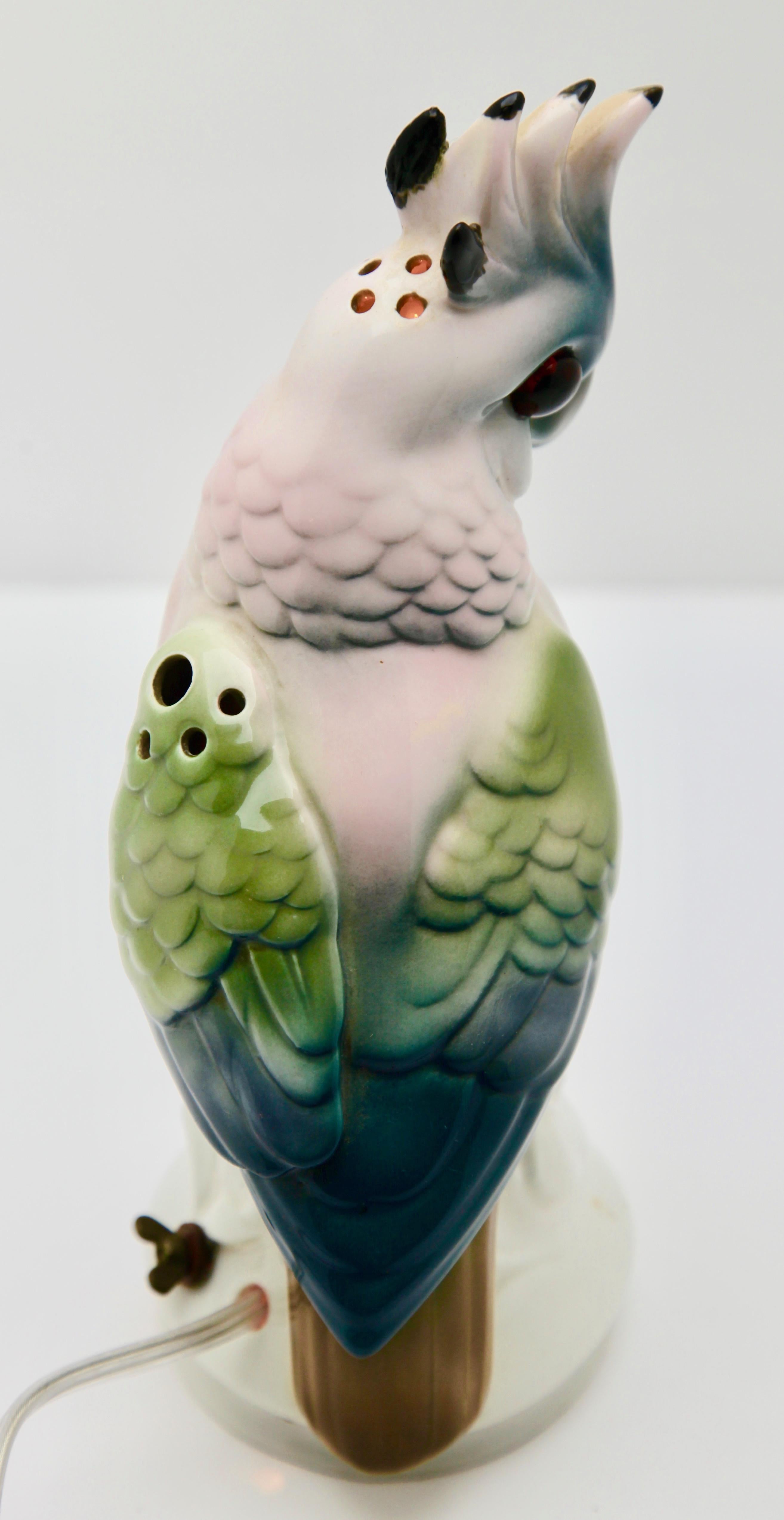 Made in Germany during the 1930s, this porcelain figurine is also an air aromiser and nightlight or table lamp.
Modelled as a cockatoo perched on a rock with hand painted plumage in blues, and greens. This friendly bedside companion features a
