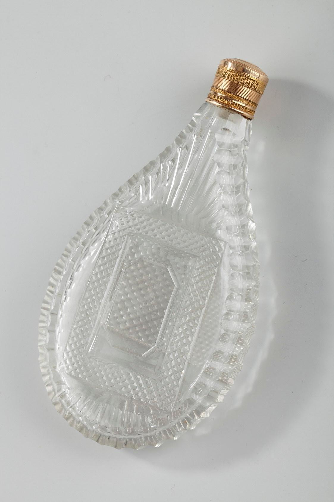 Teardrop-shaped flask in blown and cut crystal. It is embellished with several different decorative patterns: a ridged pattern surrounds the edge; the back side features a rectangular band with a diamond cut pattern and starburst rays above and