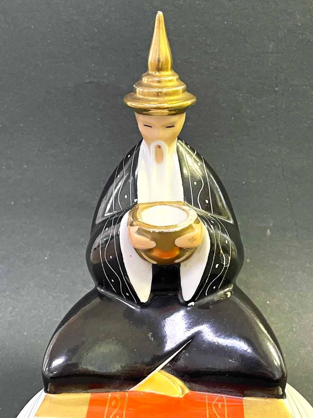 À la fois charmant et sophistiqué, ce chauffe-parfum en porcelaine - représentant un Chinois barbu, coiffé d'un chapeau pointu et vêtu d'une robe noire, au sommet d'une plate-forme à gradins - a été réalisé par ROBJ, l'un des fabricants français les