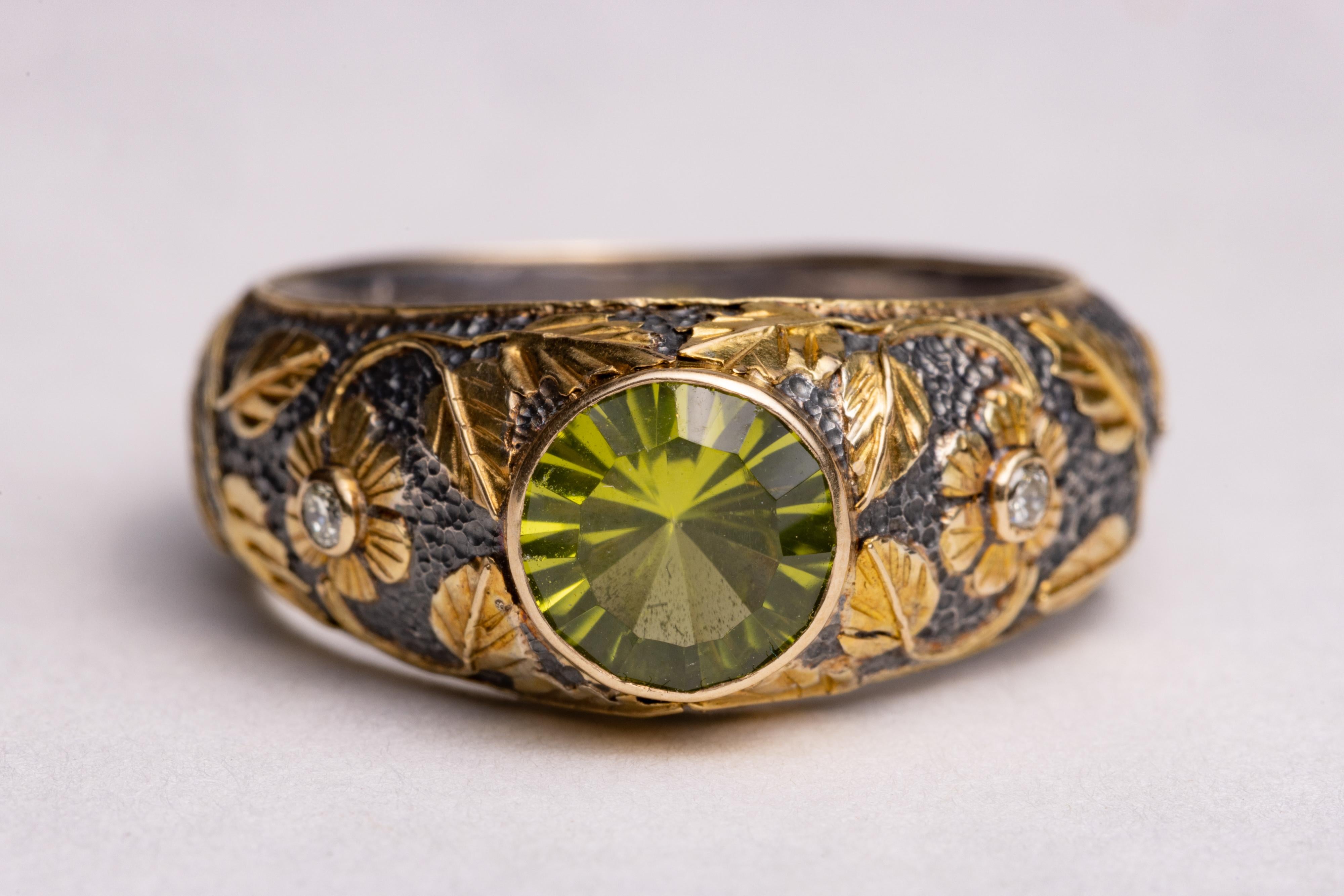 An unusual spirt sun faceted peridot gemstone ring with two round, brilliant cut diamonds on the sides creating the center of the 18K gold overland flowers and vine design.  The base of  the ring in an oxidized sterling silver. Ring size is 7.

The