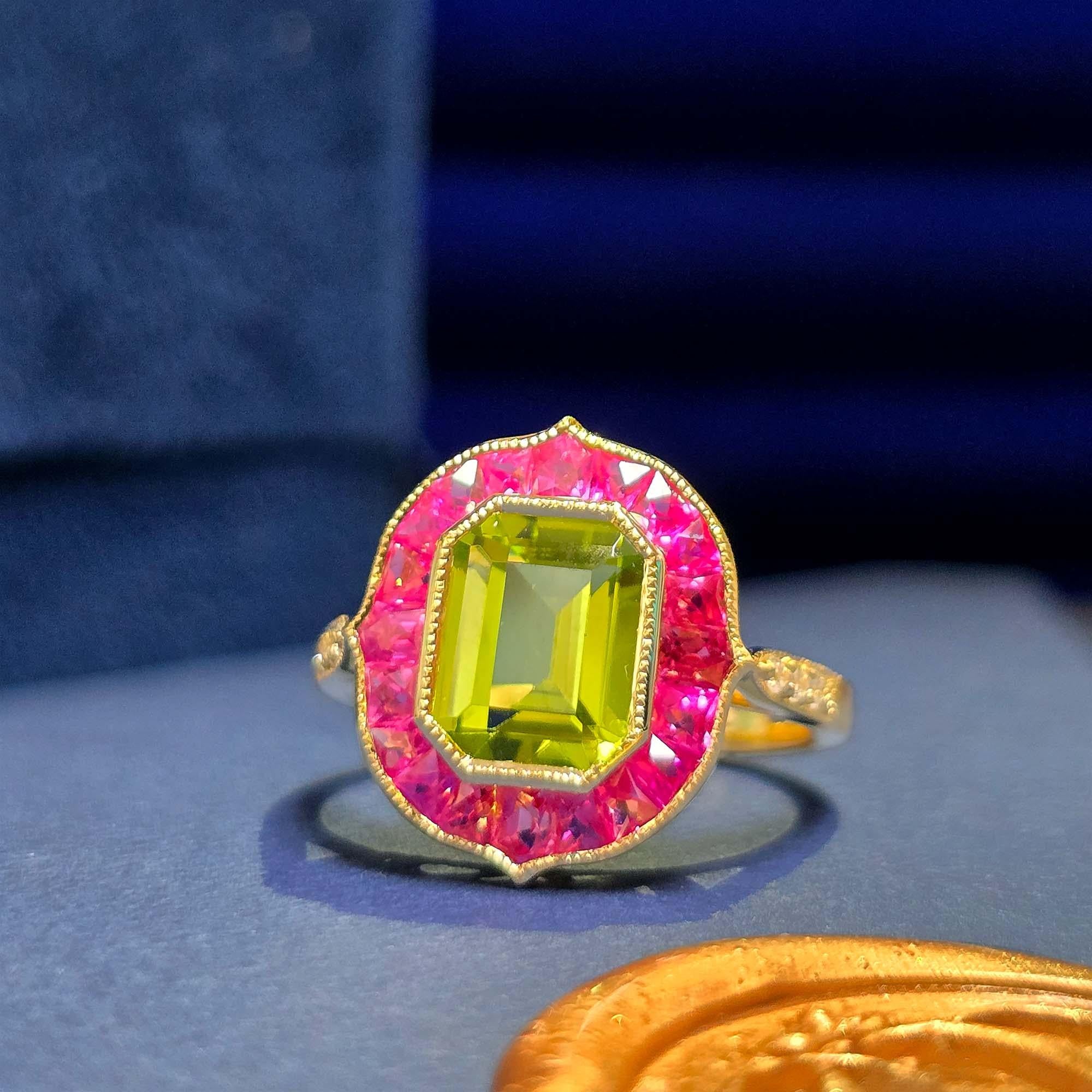 Au centre, un péridot de taille émeraude, magnifiquement encadré par des rubis rosés. Les épaules de la bague sont ornées de diamants étincelants, ajoutant élégance et brillance. L'association du péridot, du rubis et du diamant crée un design coloré