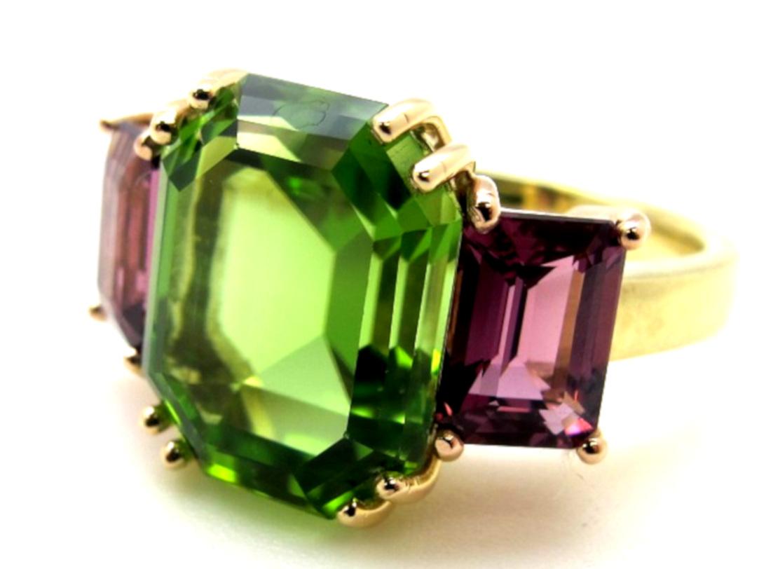 Wow! What an exciting color pairing of gemstone shapes and colors! This ring features a large, fine, grass-green peridot flanked by raspberry rhodolite garnets. The unusual cuts and fine colors of gemstones used make this an original version of the