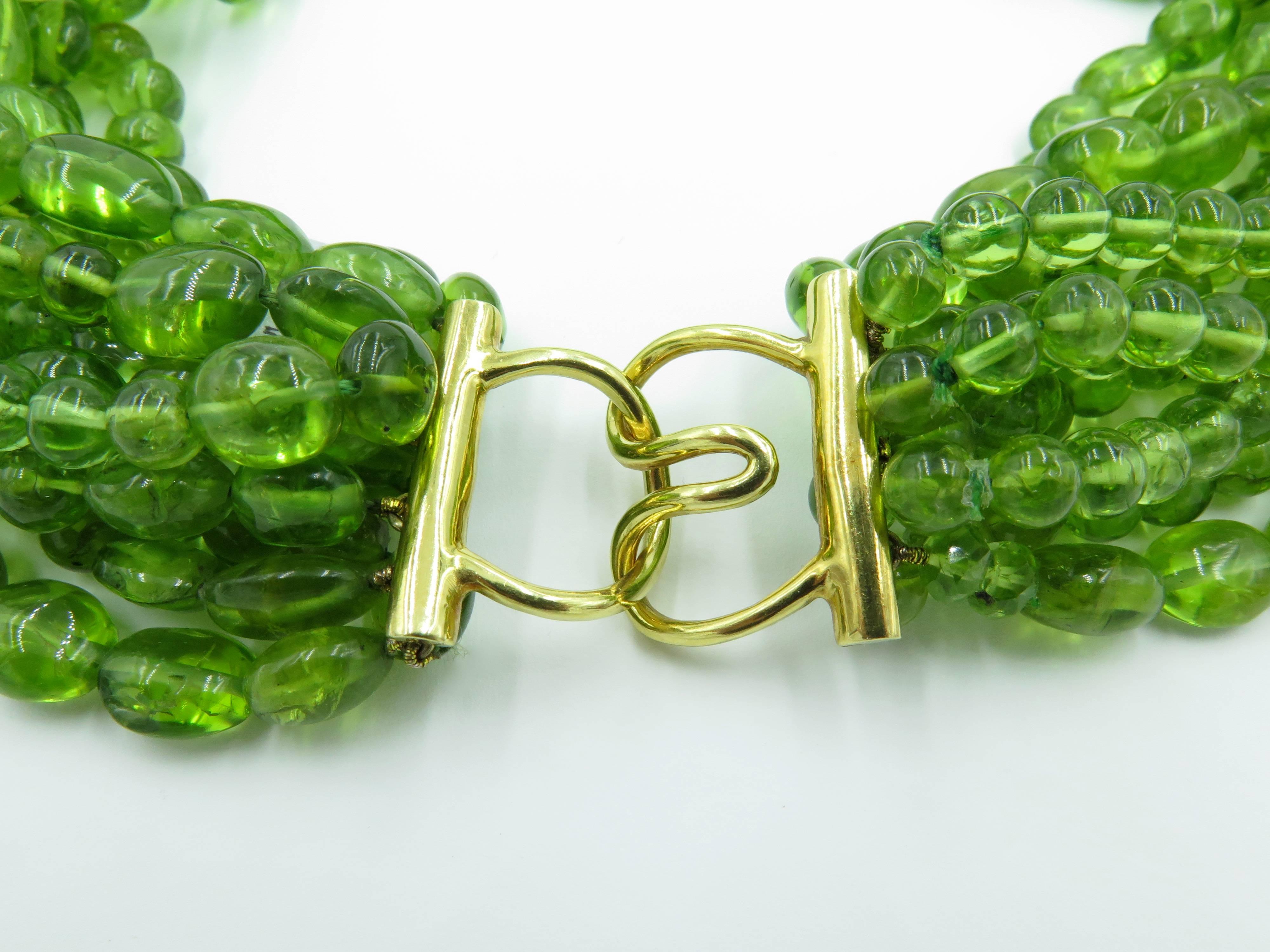 An 18 karat yellow gold and peridot bead choker. Designed as eleven strands of round and tumbled oval peridot beads, measuring from approximately 6.00-10.10mm, joined by a polished gold clasp. Length is approximately 15 inches. 