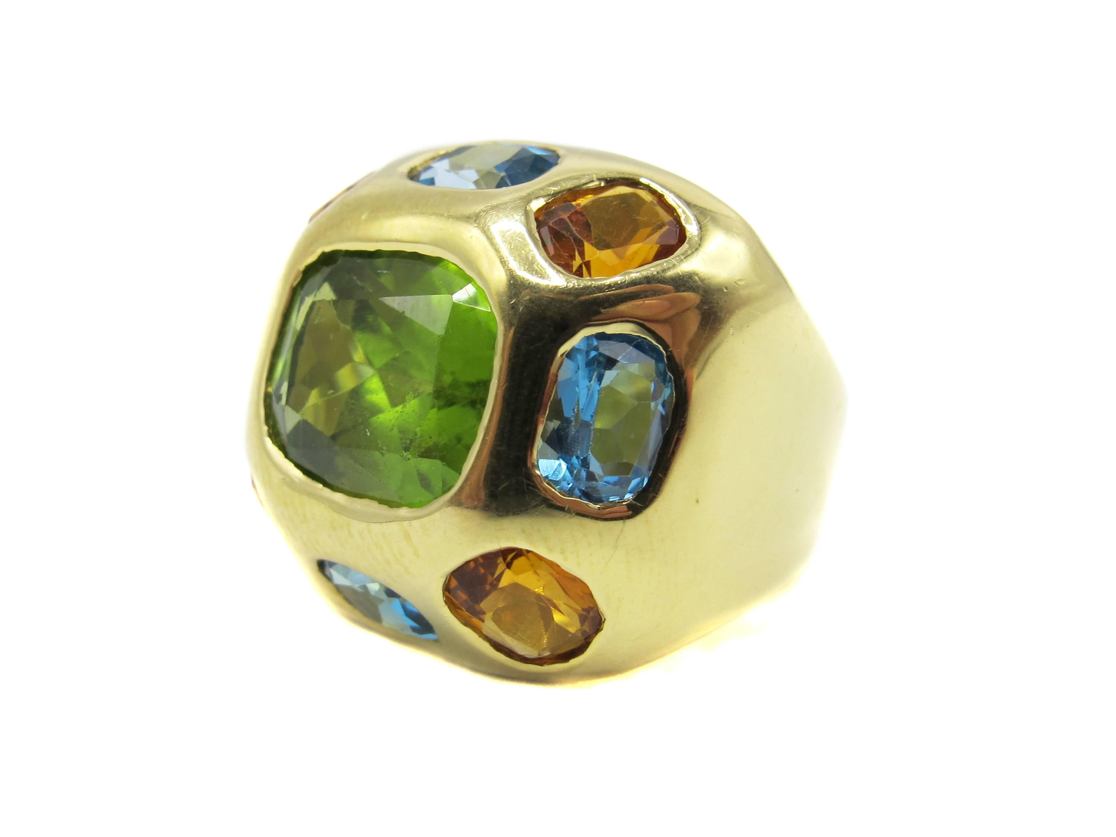 This fun and colorful 18 karat yellow gold ring displays three different lively colors with a large cushion cut Peridot in it's center, Each corner is set with golden orange Citrine and inbetween these 4 oval sky blue Topaz ovals are set flush with