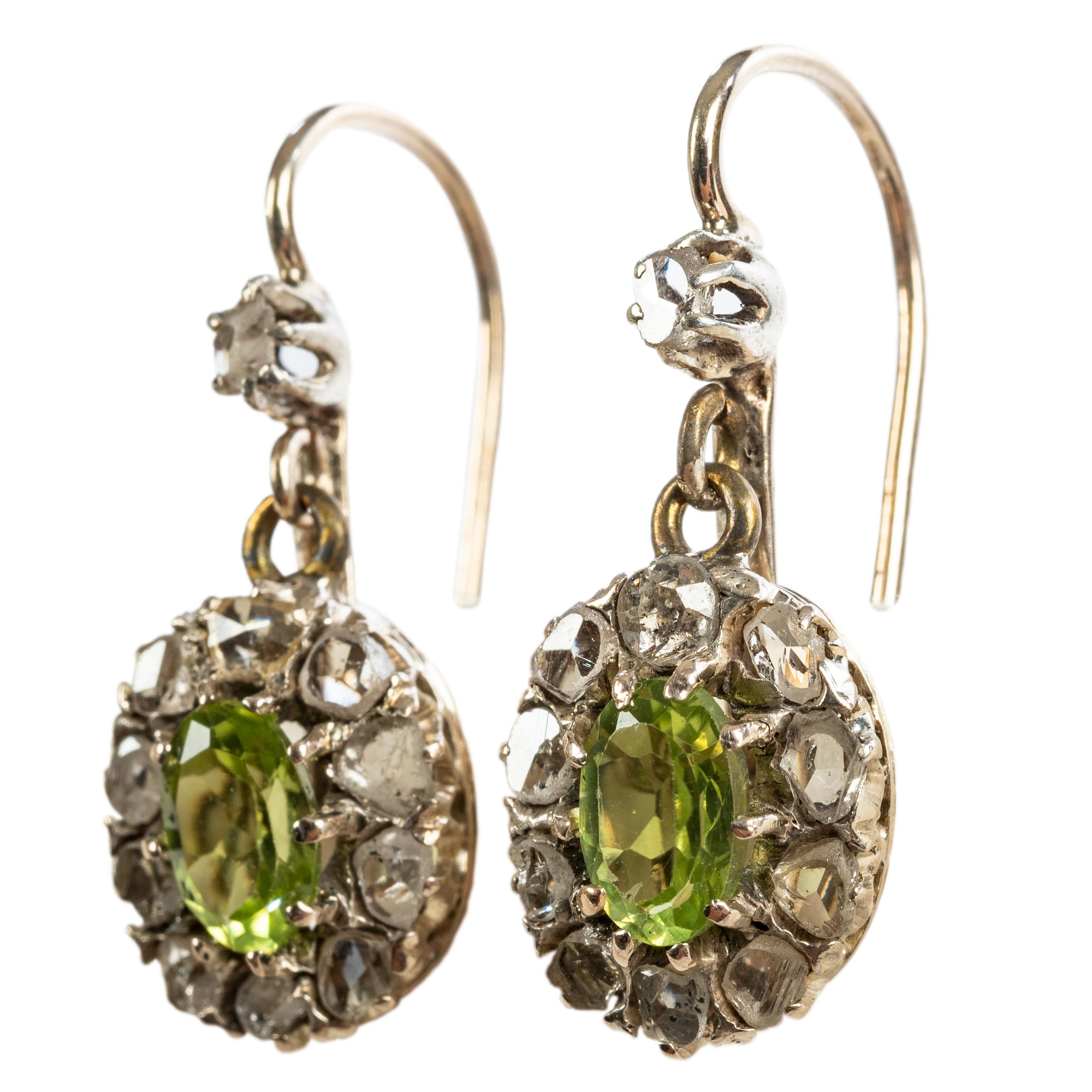 Designed as pendant earrings, each set with an oval cut peridot surrounded by ten faceted antique-cut diamonds, suspended from a single diamond, mounted in silver and gold, fitted with gold wire backs

English, 19th century

1 in. (2.5 cm) long;