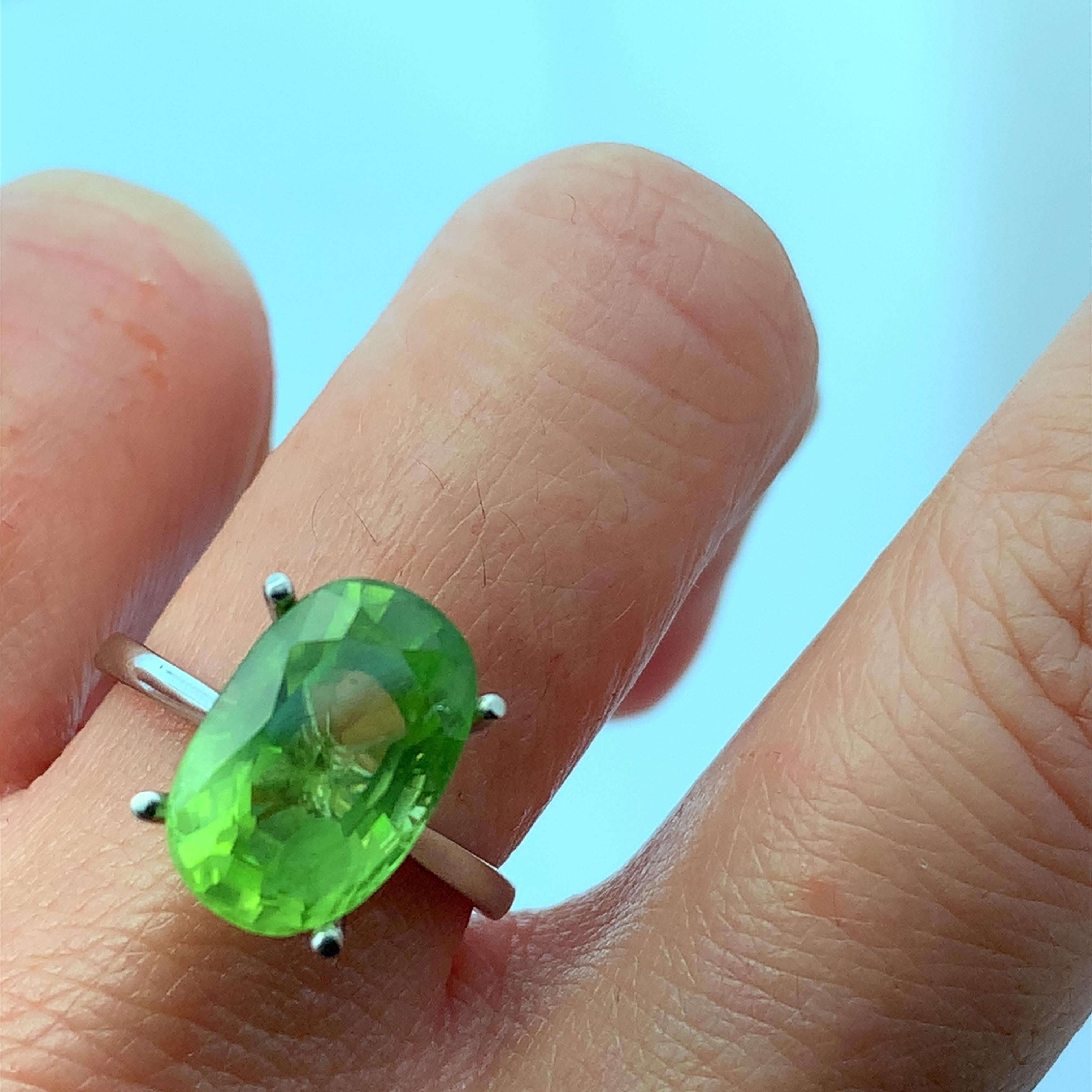 Discover the allure of this stunning green peridot gemstone ring, featuring a beautifully cut oval stone 5.50ct measuring approximately 14x9mm that captures the light with every movement. Crafted with precision, the sleek 18k white gold band