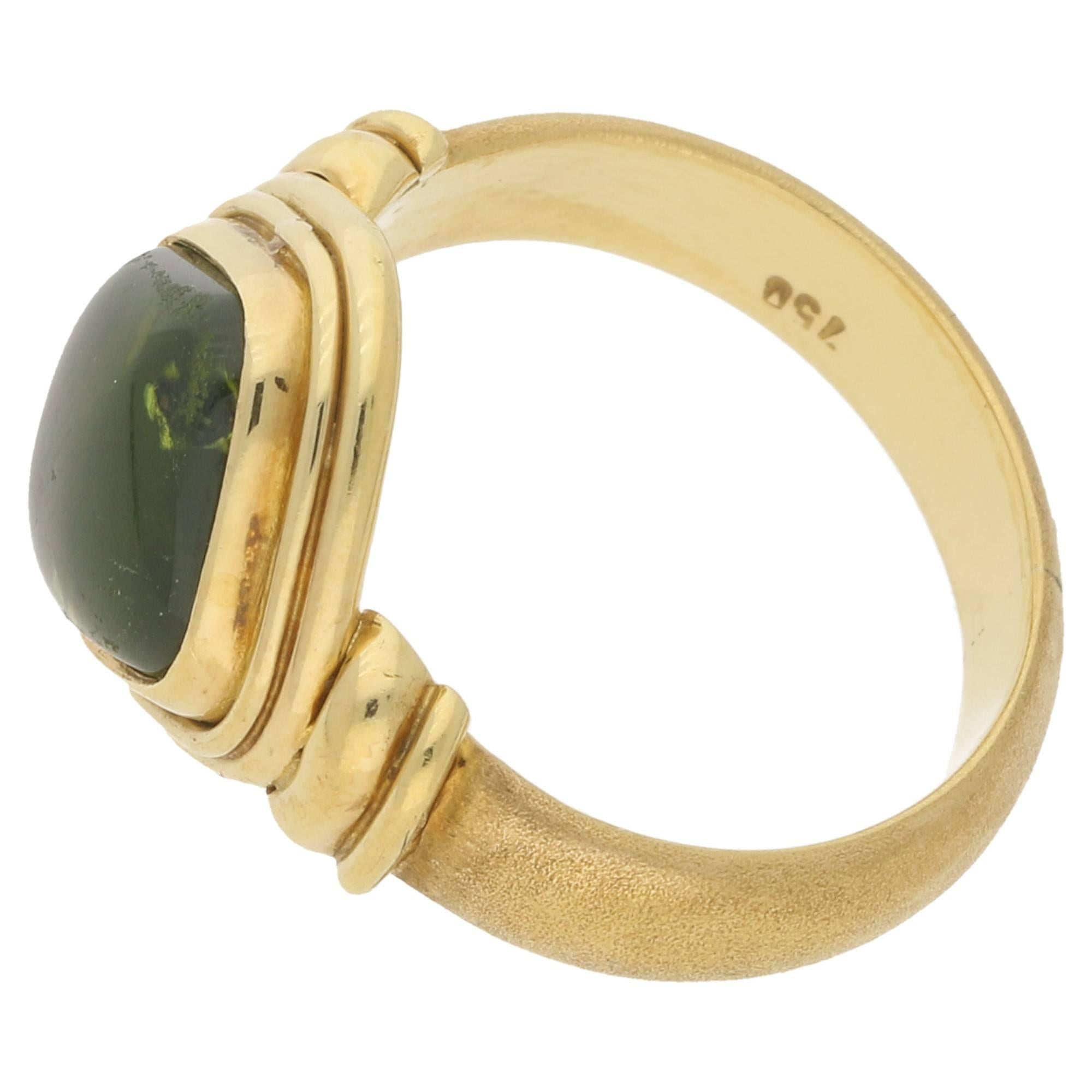 A Georgian inspired dress ring consisting of a square shaped cabochon peridot, rub-over set to the centre in a beautifully contrasting 18k yellow gold mount which is stamped 750.  

This beautiful green coloured peridot is one of those rare