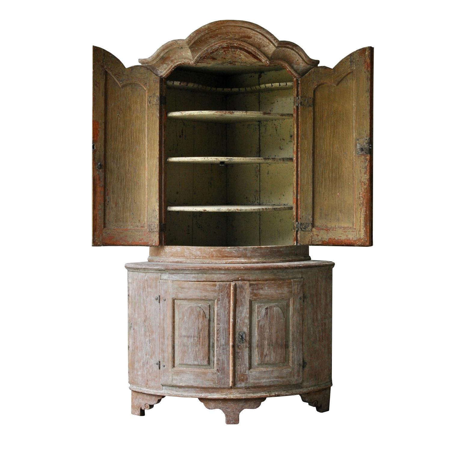 A period Rococo corner cabinet with decorative carved pediment. Two shaped carved doors open to shelved storage, and below two further doors open to more storage. Original locks and hardware. This piece has been scraped to the original paint on the