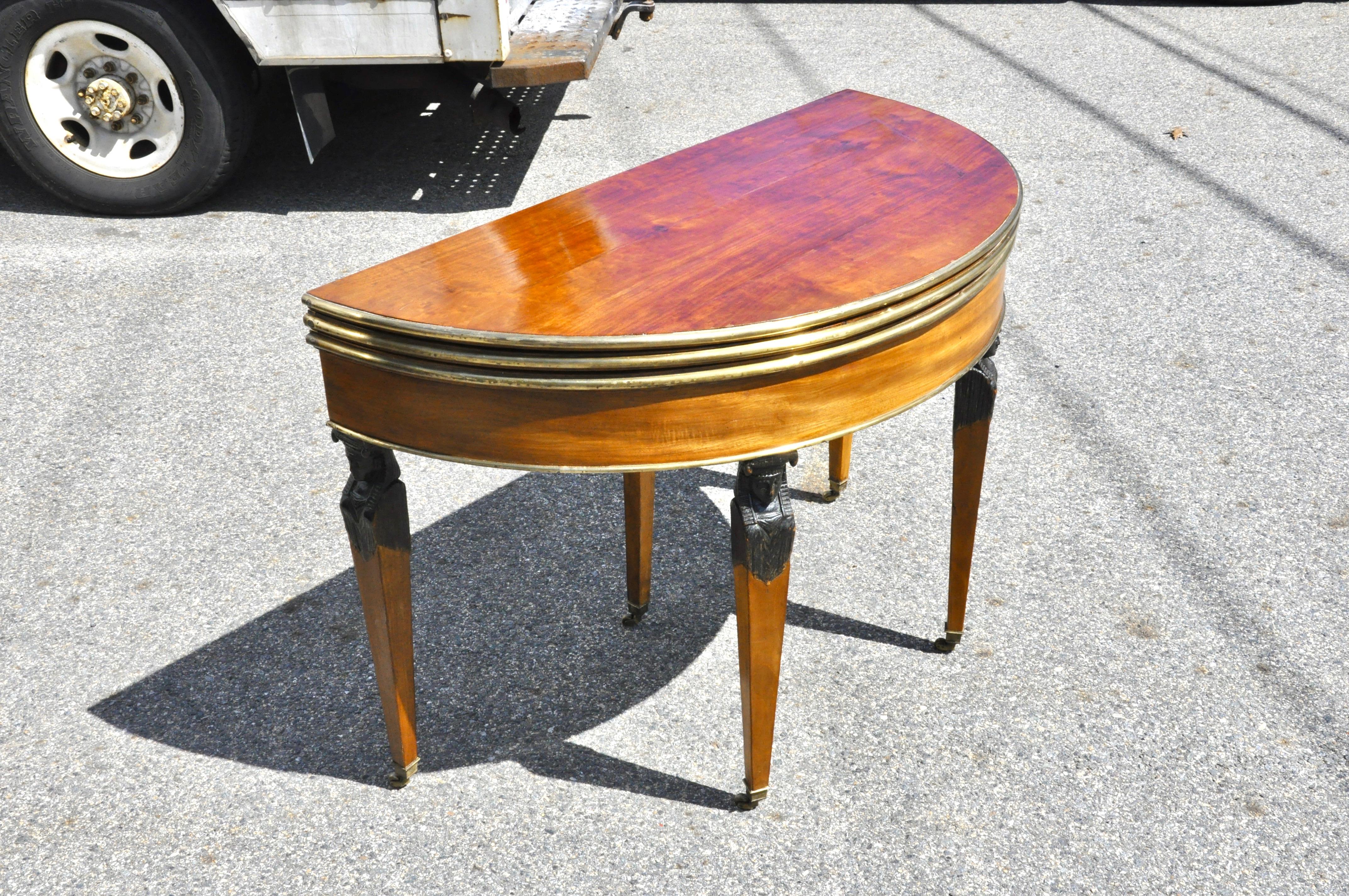 Period 18th century Russian mahogany flip top card table.

-- Demilune opens to mahogany round table or a third flip to a felt covered card table
-- Exquisite wood
-- Egyptian neoclassical caryatid legs
-- Brass bound
-- Opens to a mahogany