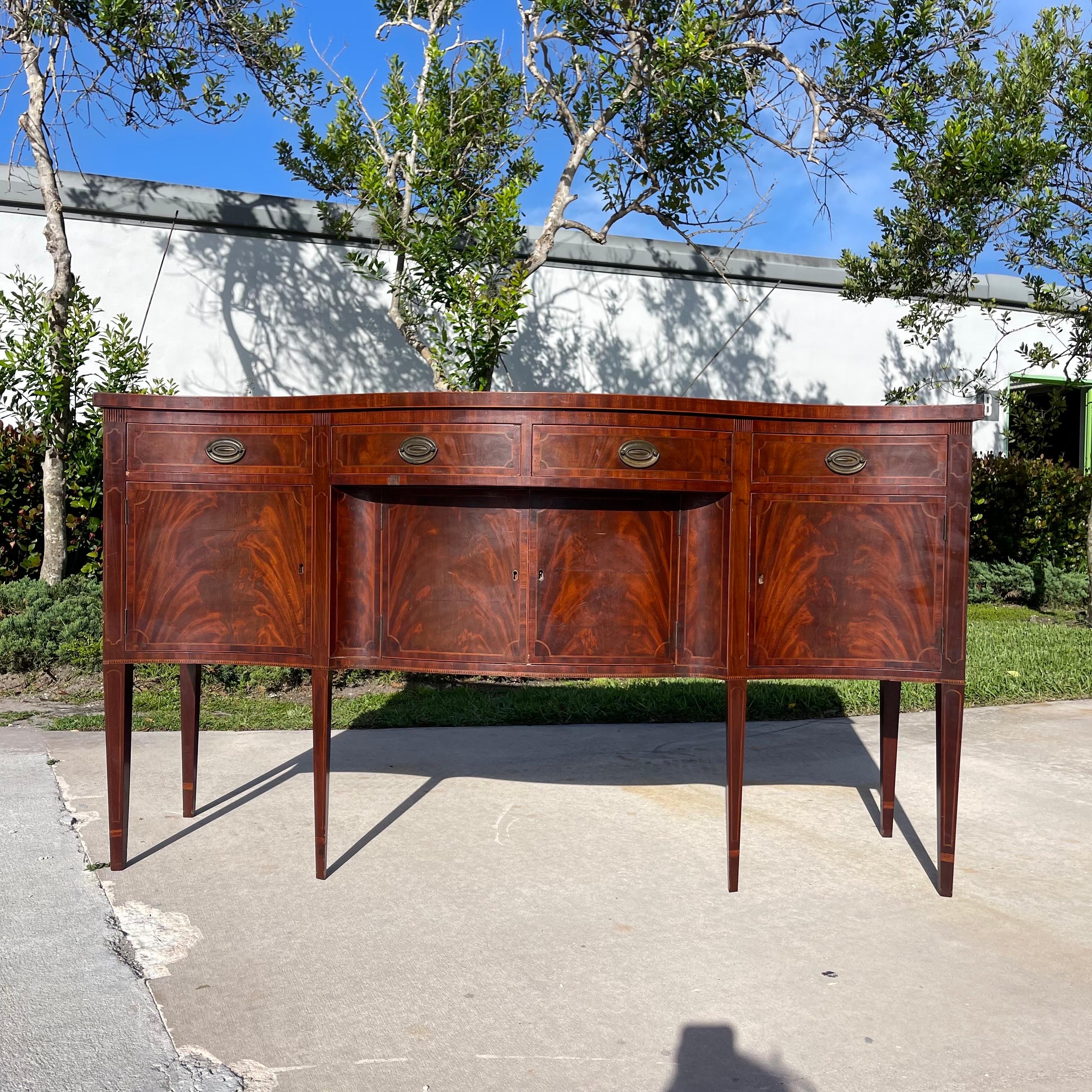 Splendida credenza a serpentina in stile federale, con impiallacciatura in mogano a fiamma e intarsi a motivi. Venduto non restaurato con patina e perdite originali. Un'ottima ossatura per un restauro completo, se preferisci. 