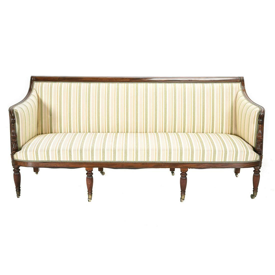 Period Antique American Massachusetts Federal Carved Mahogany Sofa. Curved and scrolled crest rail, with the arm rests terminating in carved pineapples and bulbs, set on fluted legs with brass casters, vertical stripe upholstery. Circa 1800. Solid