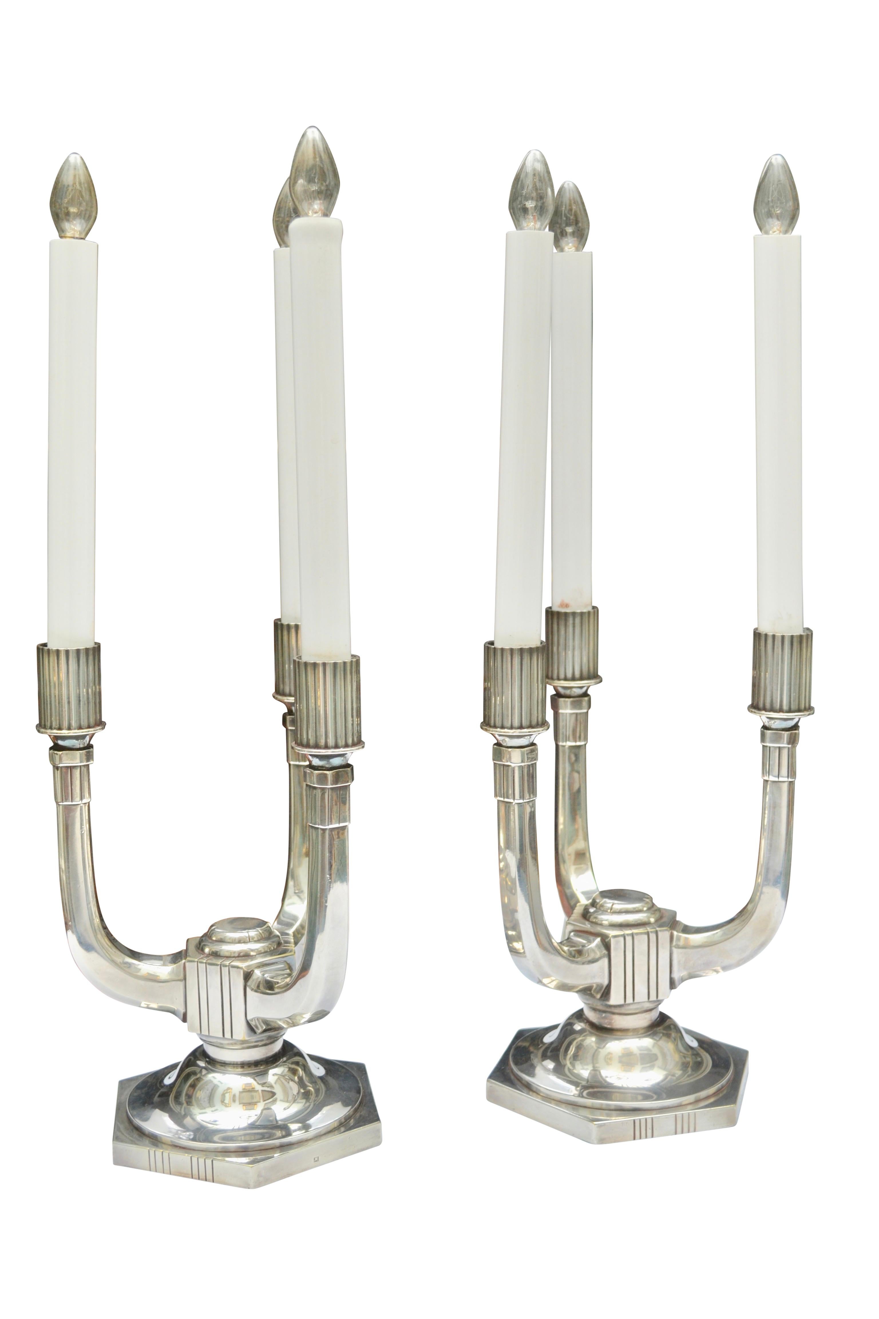 Three vertical candle arms rise from a hexagonal base. The lamps/sticks are hallmarked with a heart symbol and the letters O and E on either side of the heart symbol. Other hallmarks on the base consist of a capital C and the number 25 inset in