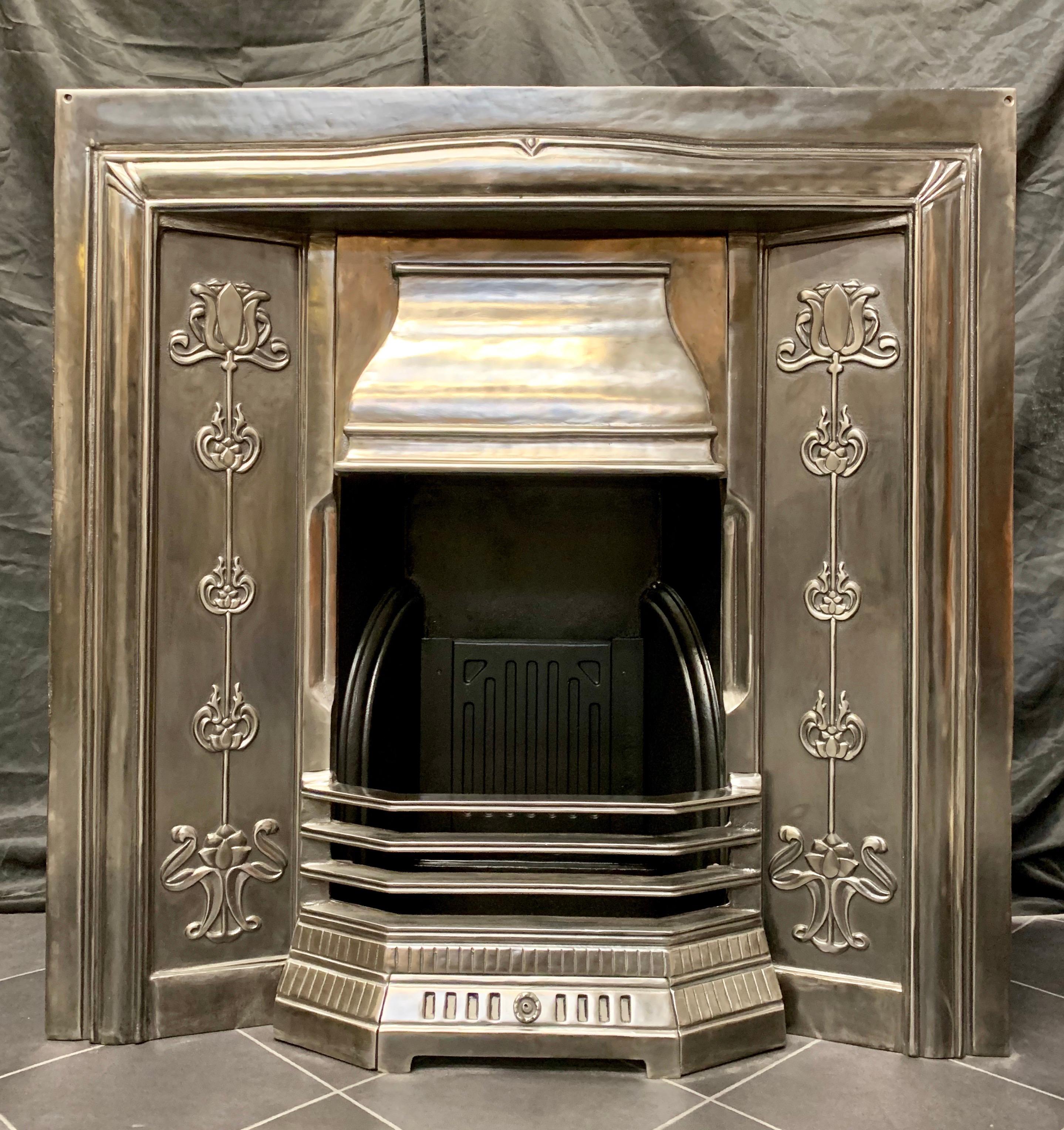 A charming and fully restored period Art Nouveau manor polished steel fireplace insert. A gently shaped top frame with cast decorative corners, the central scalloped shaped canopy, flanked by a pair of full height cast iron tiles showing Classic Art