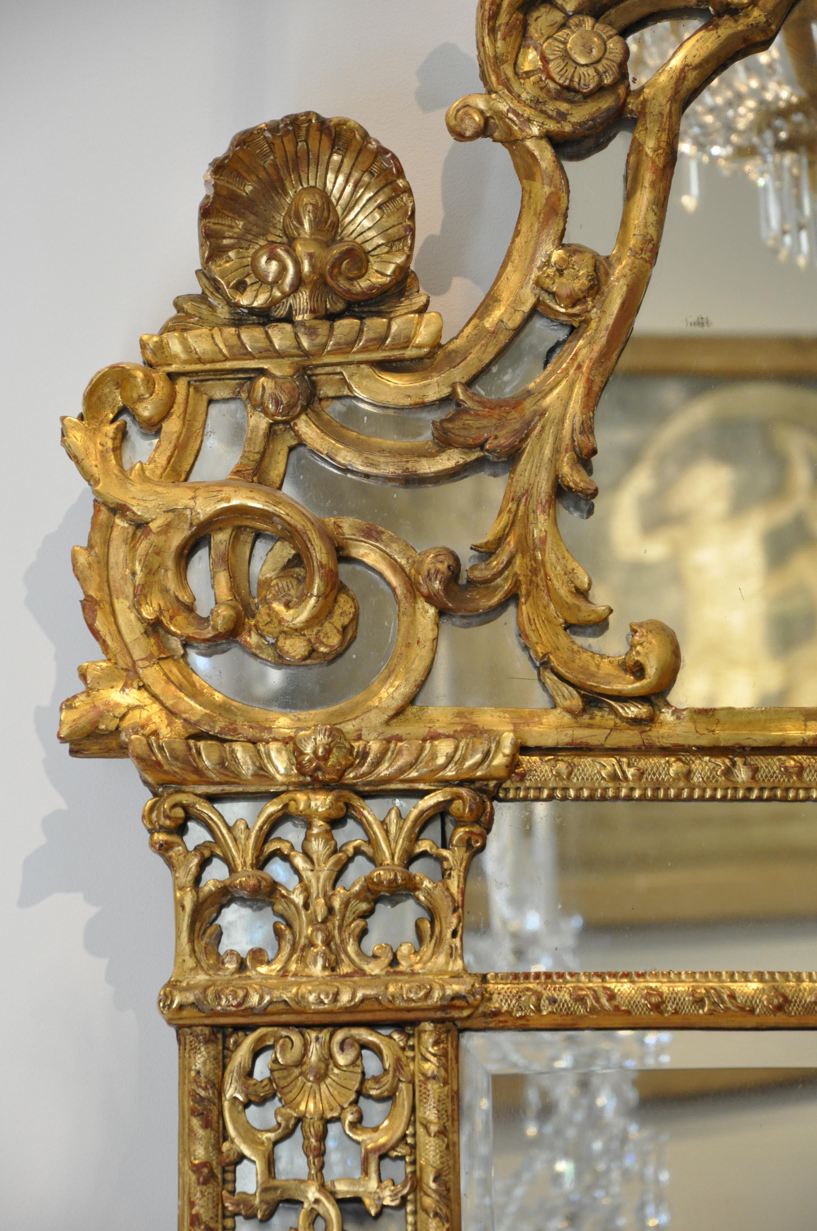 Period early 18th century French giltwood Regence mirror

In two parts with stylized carved pillars, shell motif, Regence head crowned with feathers. Early and mostly original mirror plate. Original Gilding.