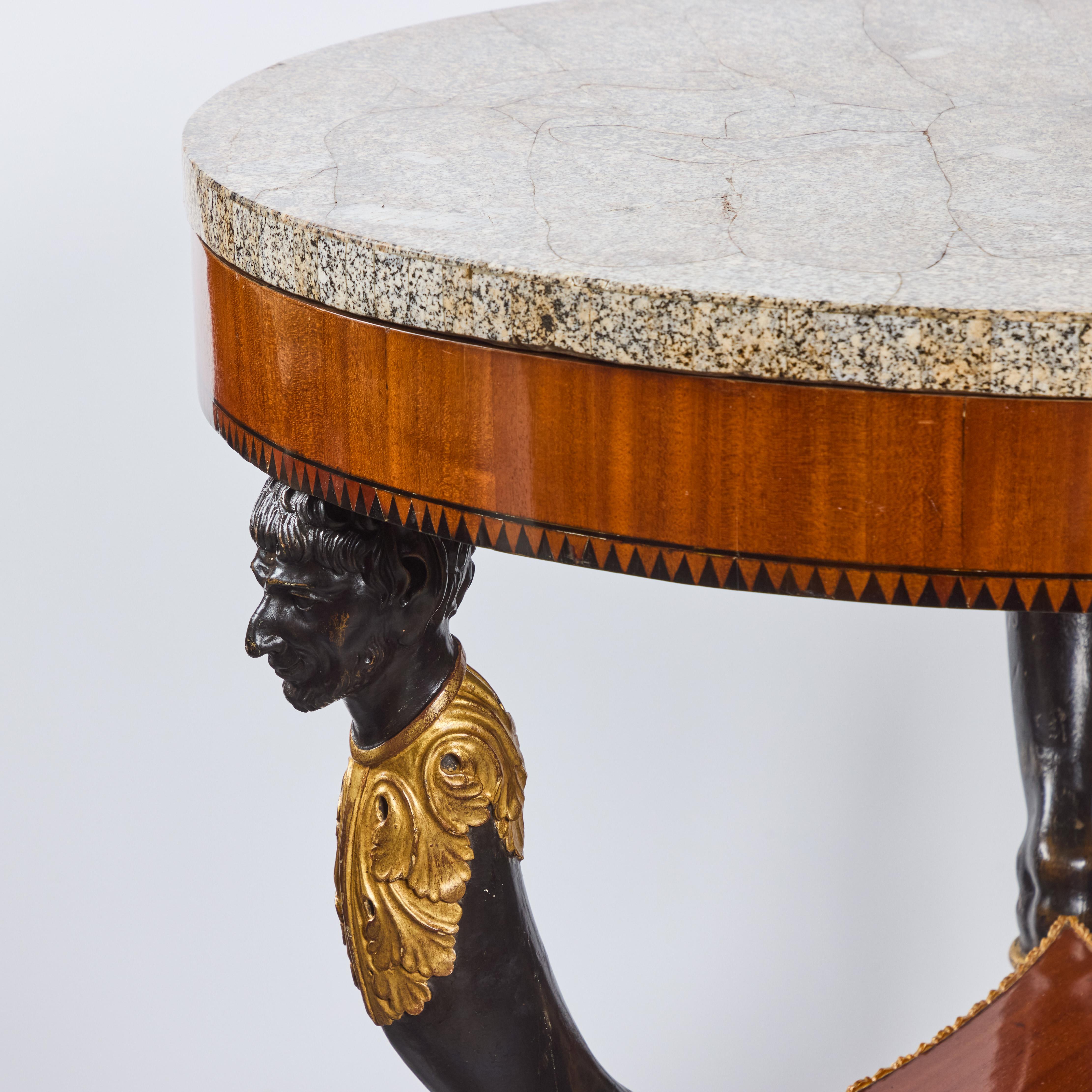 Un bellissimo tavolo gueridon d'epoca Impero impiallacciato, ebanizzato e dorato, con piano in marmo e gambe figurative che terminano con zoccoli di capra.