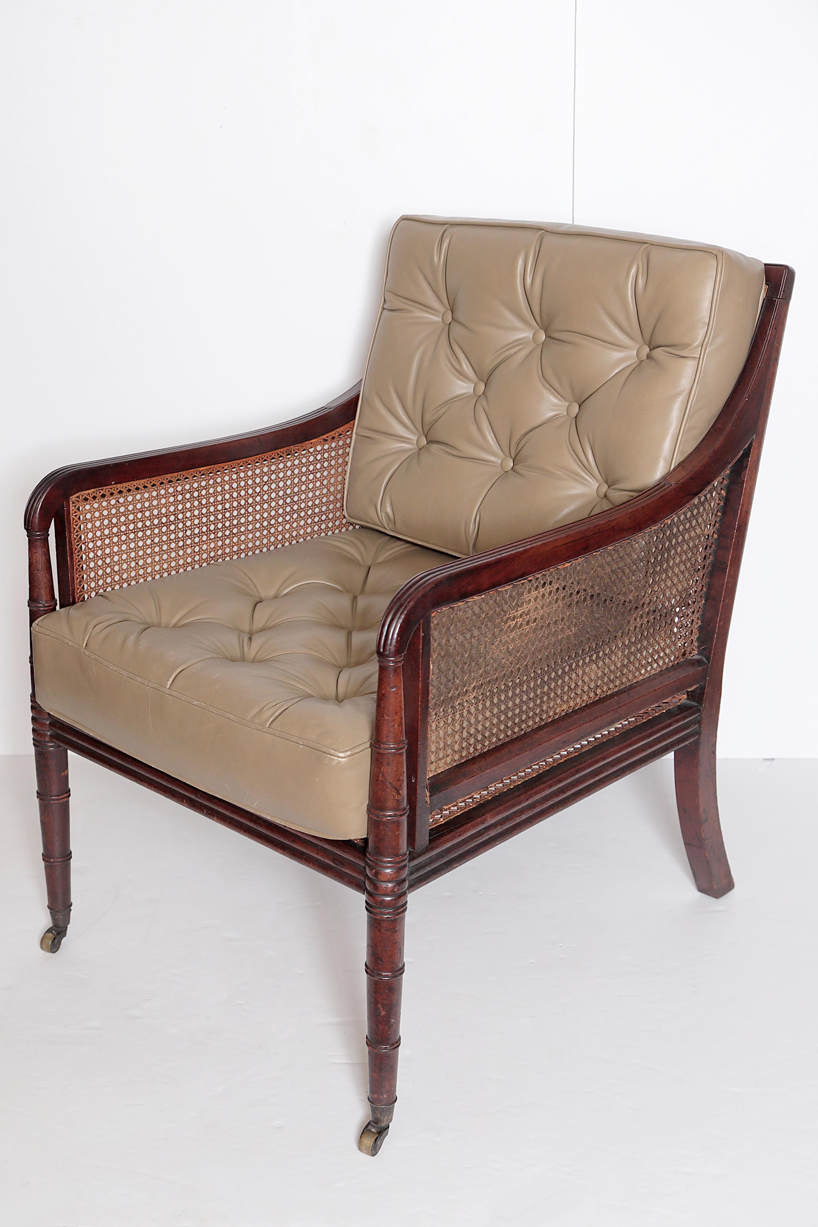 a period English Regency armchair with mahogany faux bamboo frame, caned seat, sides, and back, with olive green leather button-tufted cushions, brass castors on front legs, England, circa 1820

Measures: height of arms 26