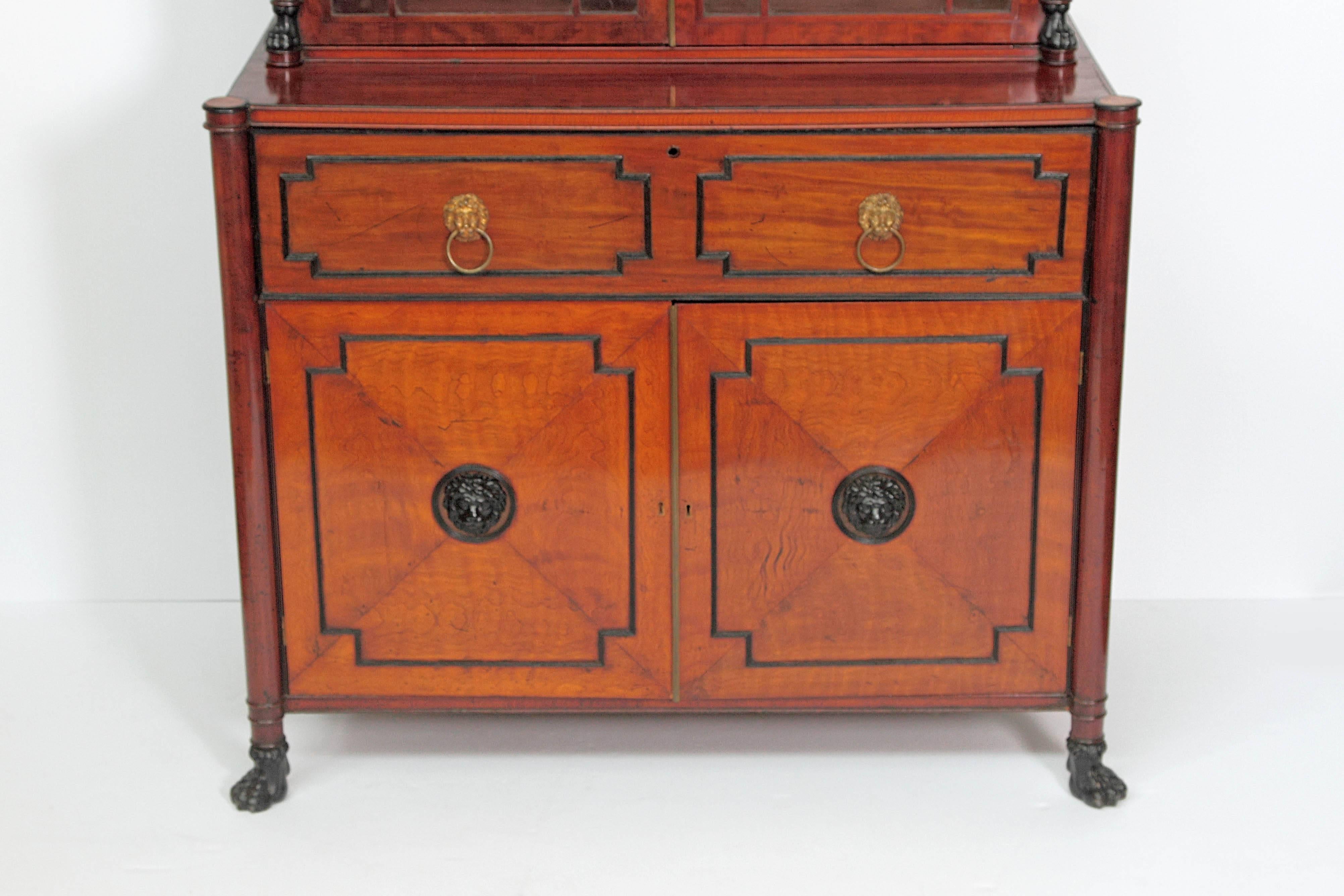English Regency period mahogany and satinwood two-piece secretary cabinet. Pine secondary wood. Top section having a shaped cornice with an ebonized lion medallion flanked by sphinxes to the center and ebonized lion masks to the corners, over an