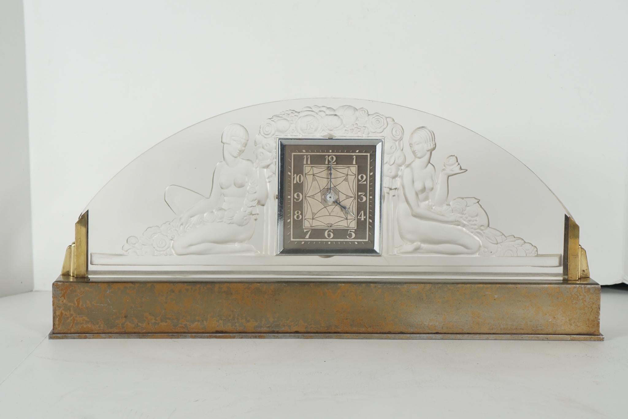 This fine period French clock was manufactured by the Sabino firm most likely before 1935. It prominently features two female nude figures lounging on either side of the inset silvered clock topped by a deco stylized garden of roses. This glass