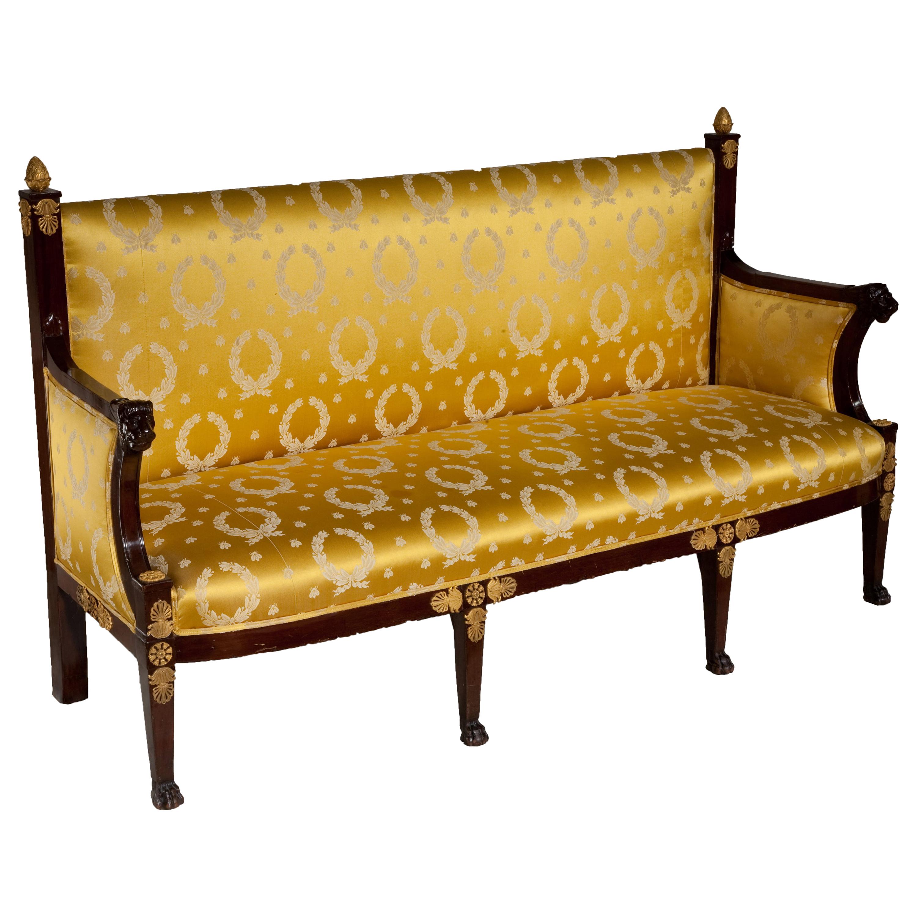A Classic Directoire mahogany cannape with lion's head arm supports and paw feet, accented by Empire ormolu mounts and upholstered in gold Empire style silk yellow fabric.