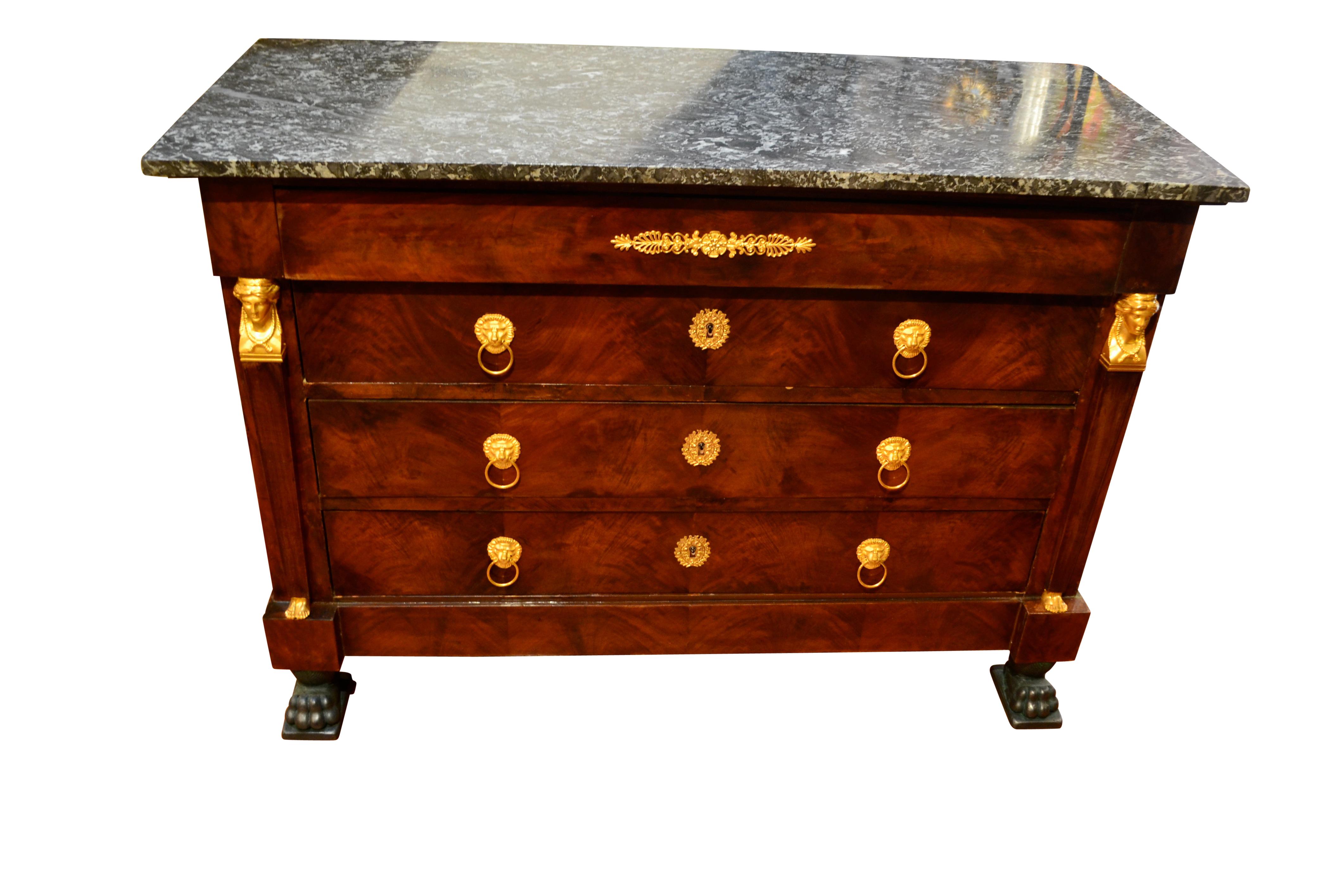 A fine example of a French Empire mahogany commode embellished with gilded bronze mounts. The commode has its original grey fossil marble top above a narrow drawer, above three larger pull out drawers, each with gilded lion’s head handles and gilded