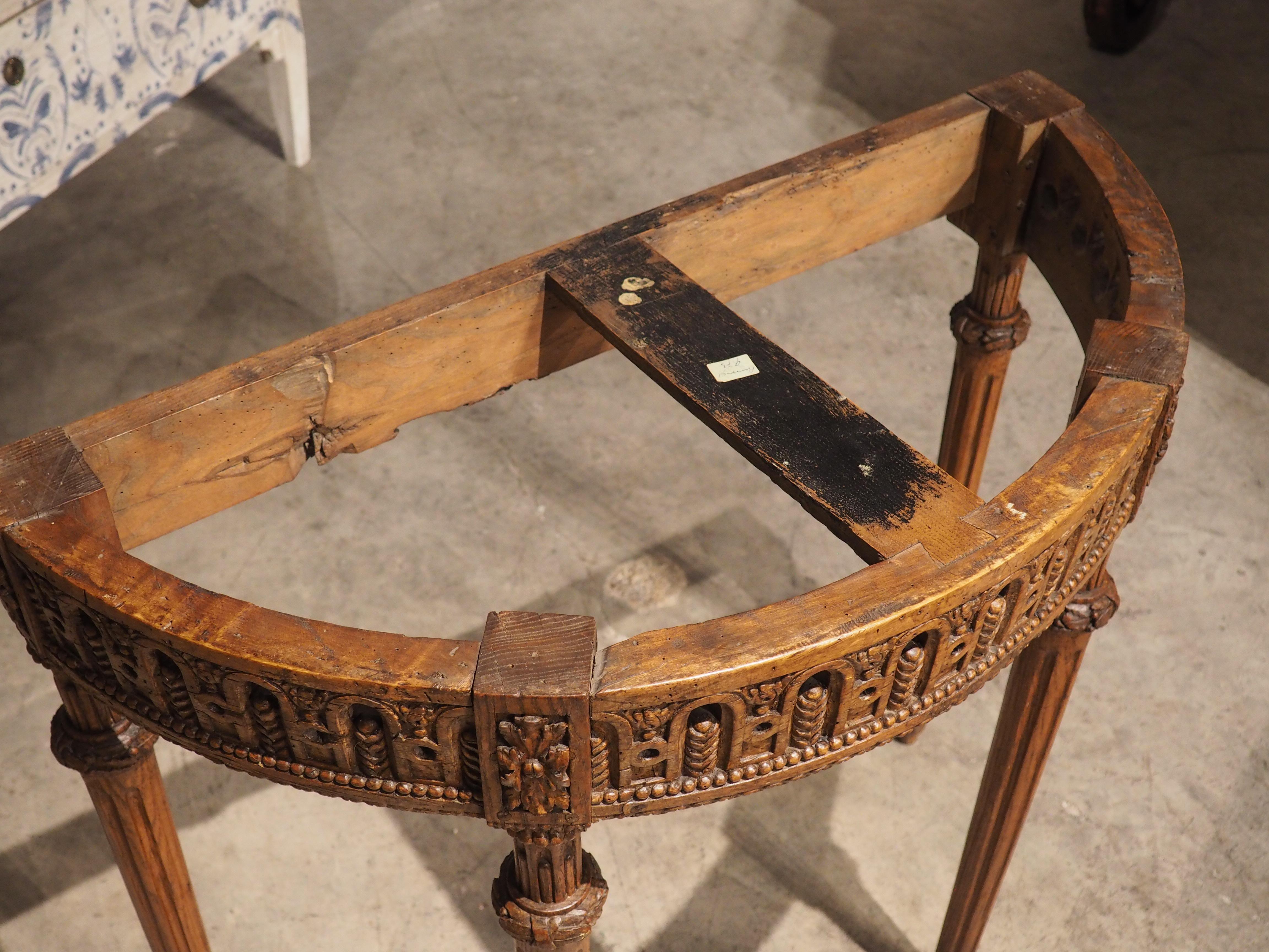 Hand-carved during the Louis XVI period, circa 1785, this oak demi-lune console is topped by a reddish brown marble with gray, black, and cream veining. Typical of tables from this era, the ¾” inch-thick marble is supported by four slender